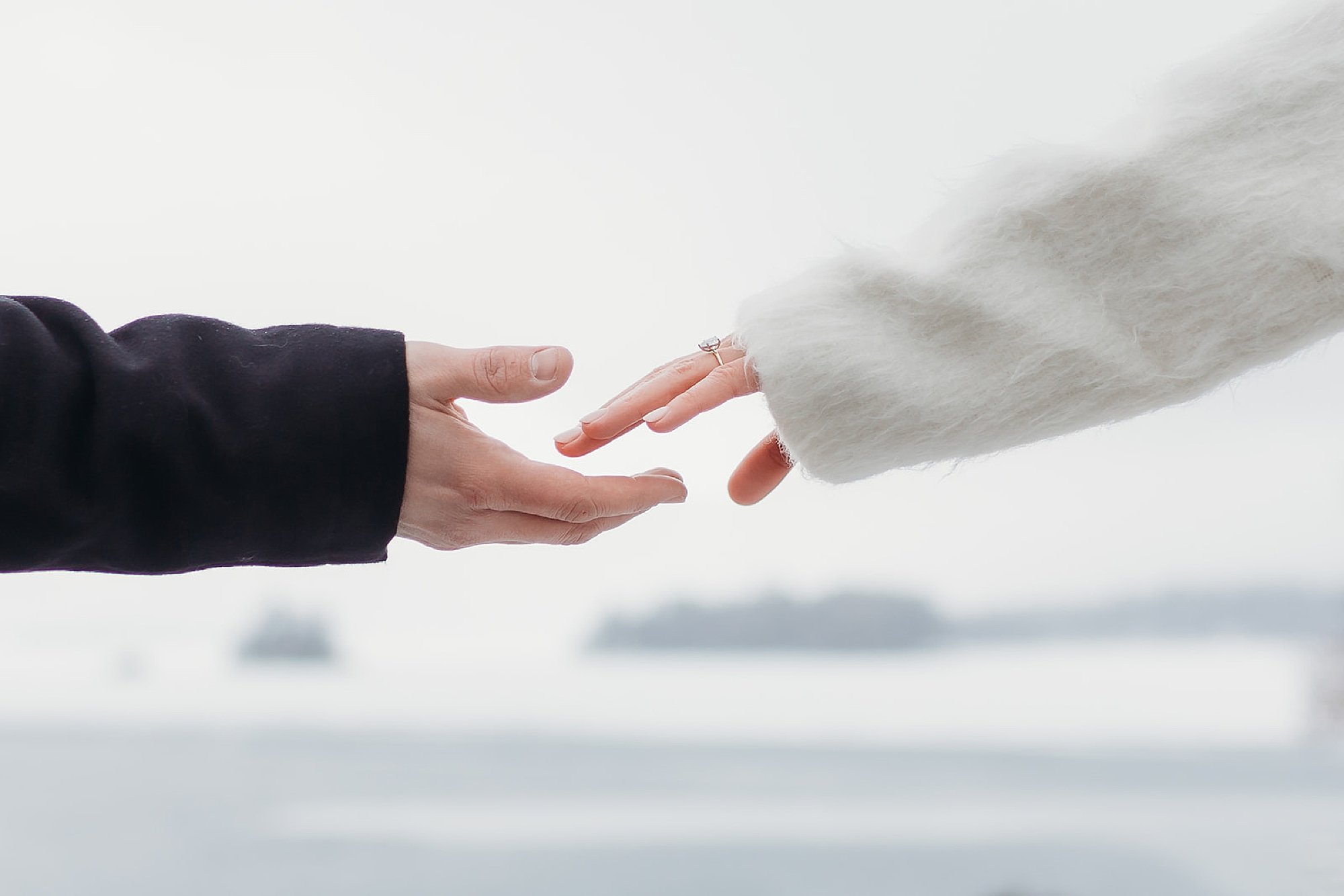 couple reaches to hold hands in winter jackets during snowy engagement portraits 