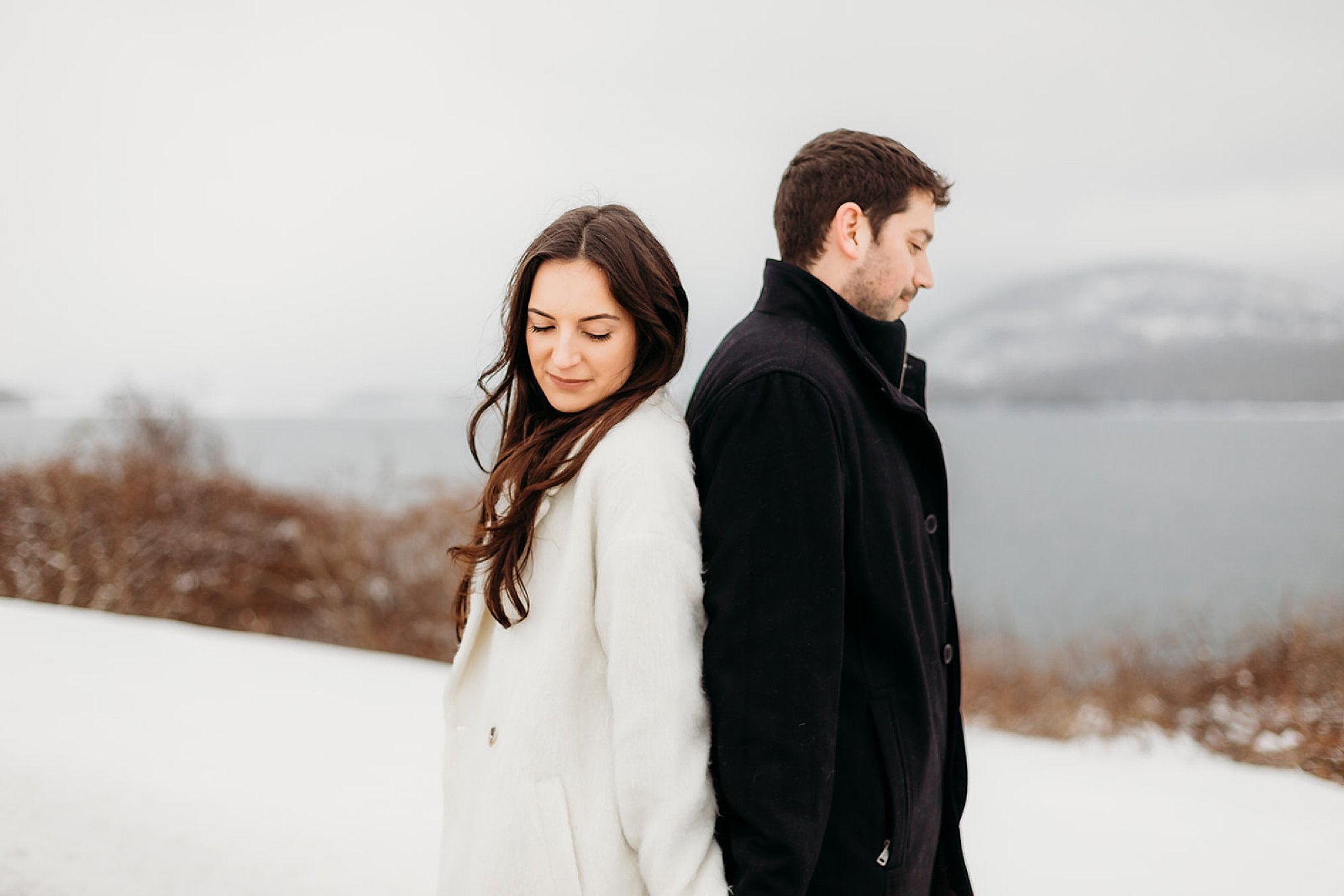 couple stands back to back in winter jackets on snowy hill at The Sagamore Resort