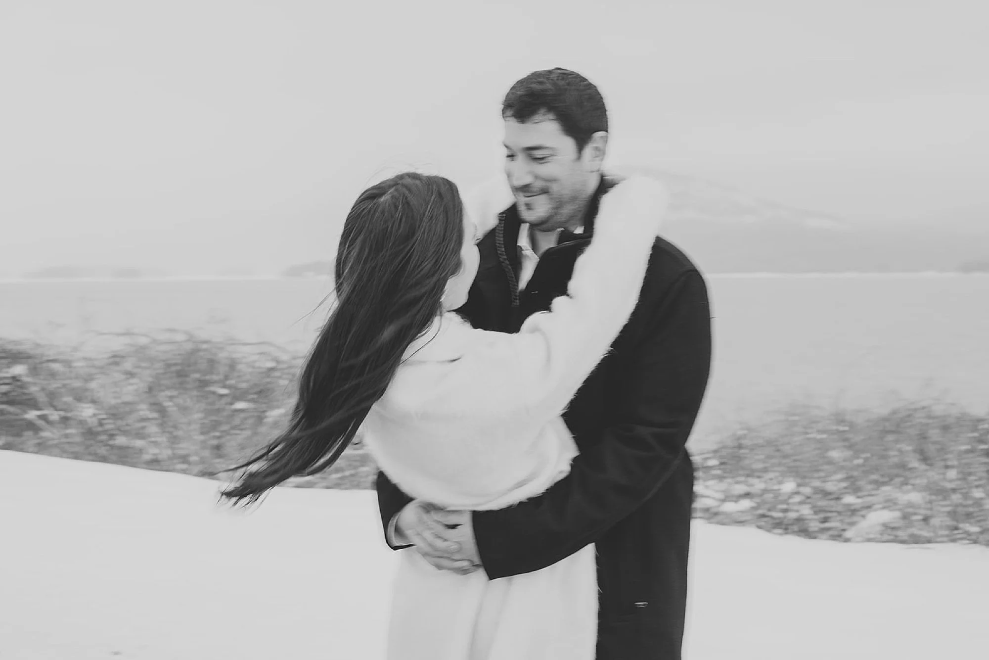 man twirls woman around in snow on Lake George 