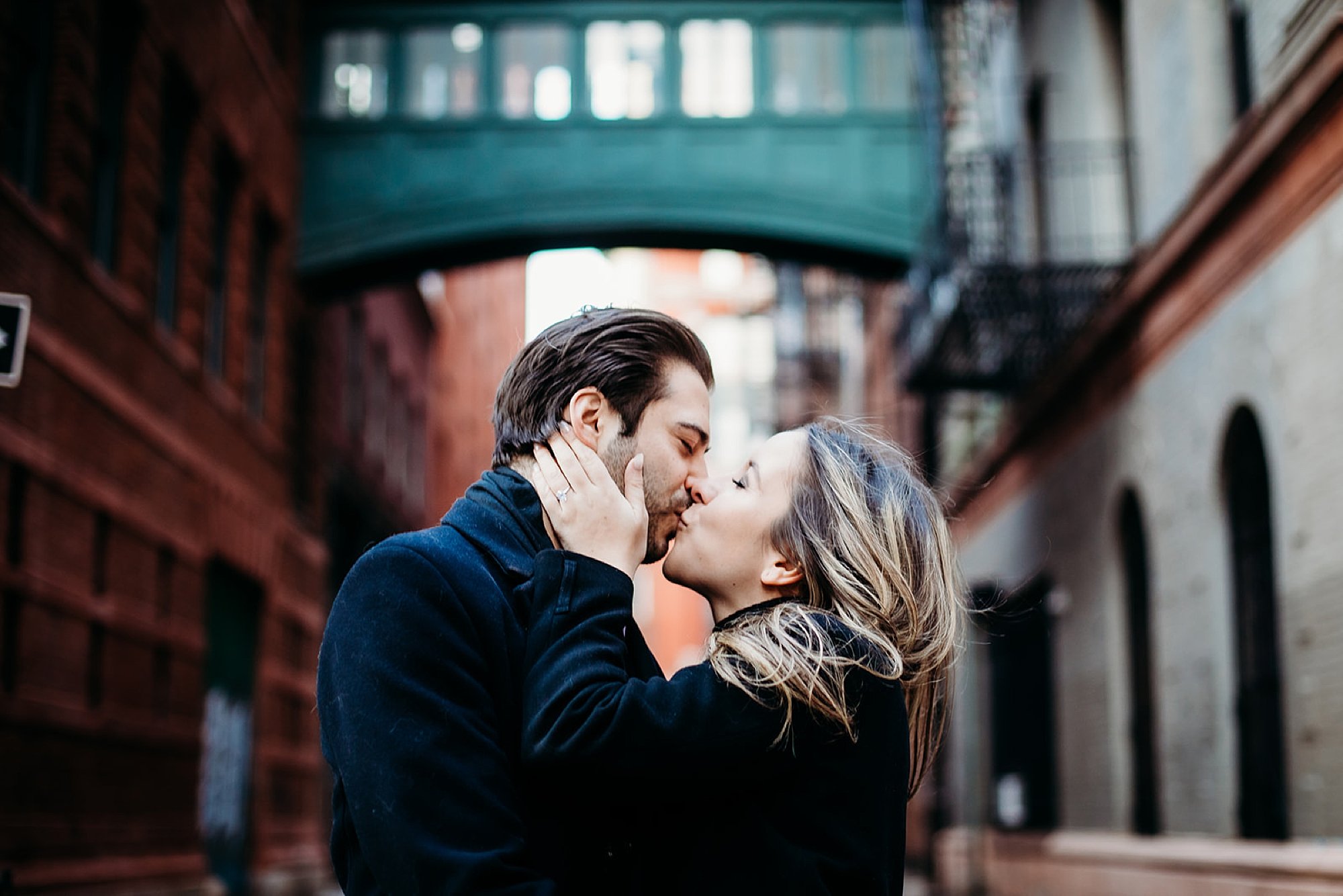 woman kisses man holding his jaw with teal floating bridge behind them