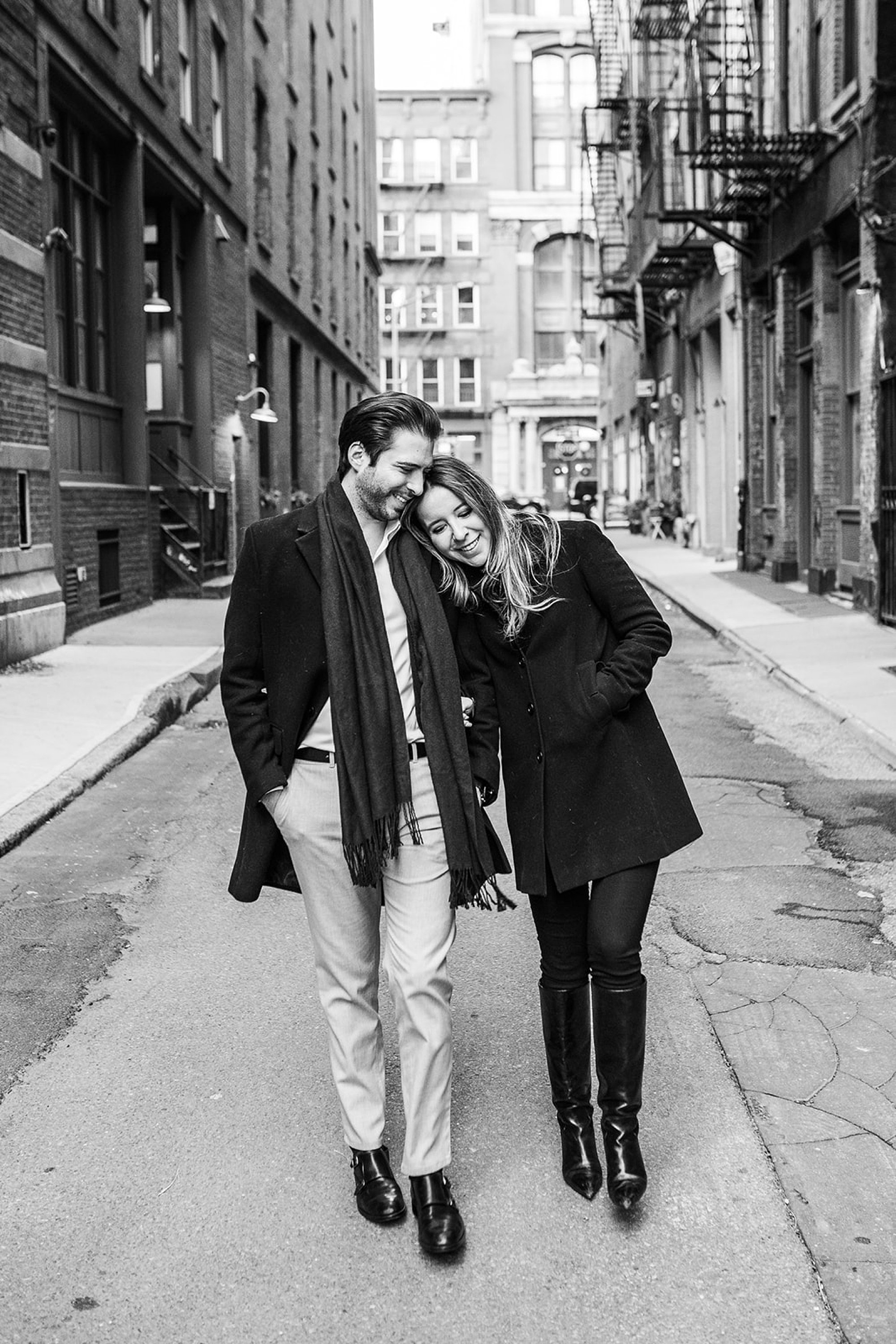 black and white portrait of woman leaning head on man's shoulder walking down sidewalk 