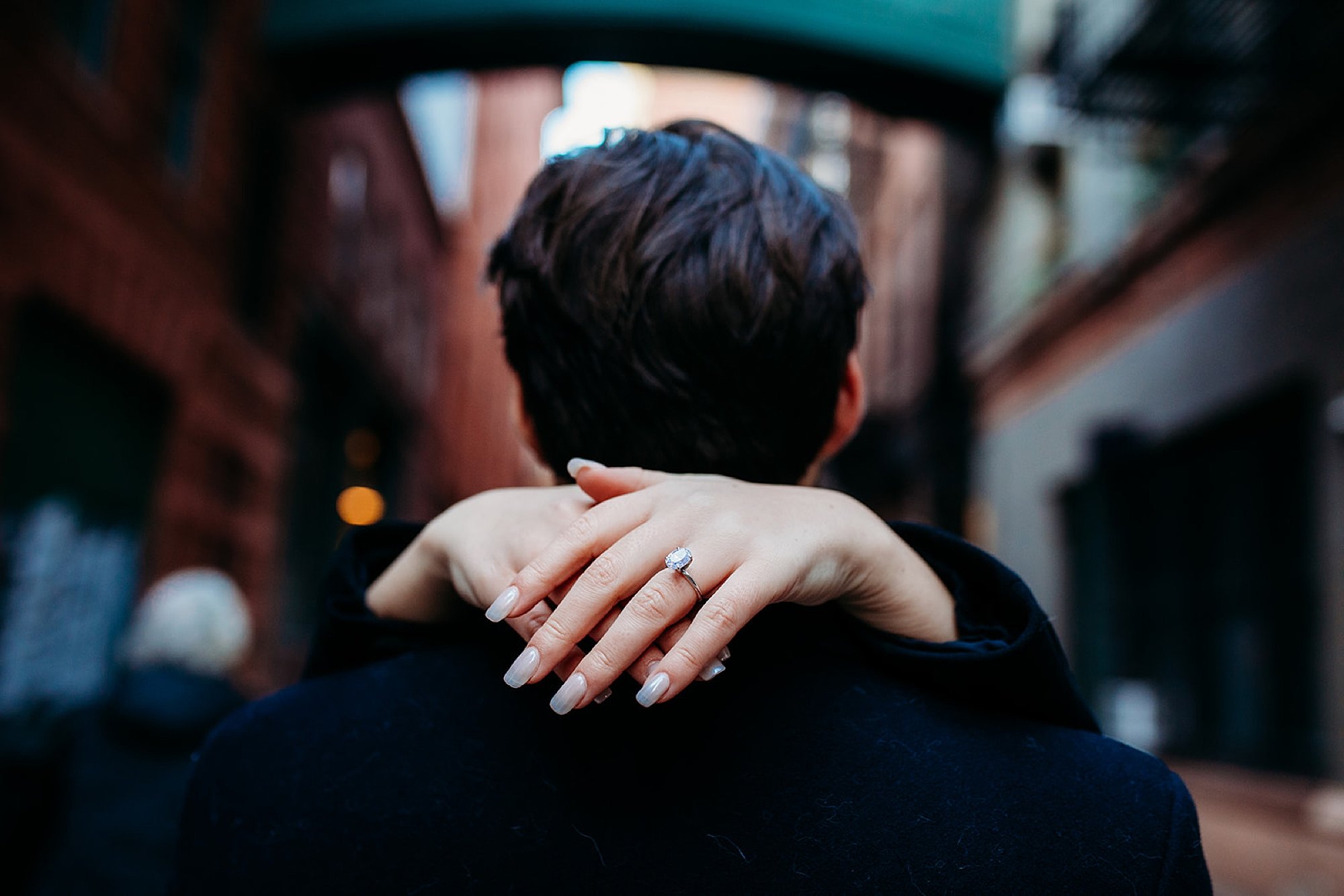 woman hugs man around neck showing off ring