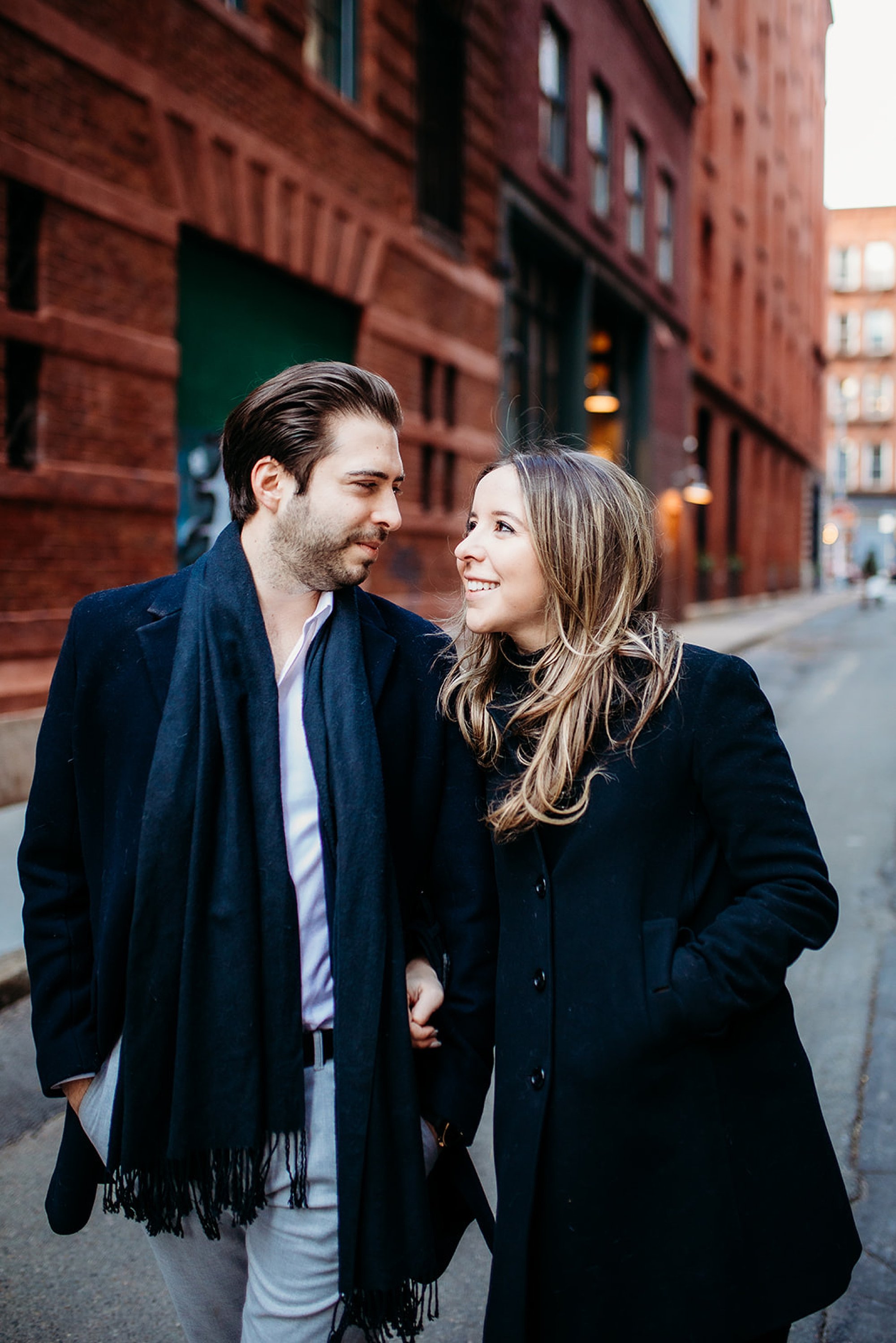 couple looks together and smiles during winter engagement session in Tribeca NY