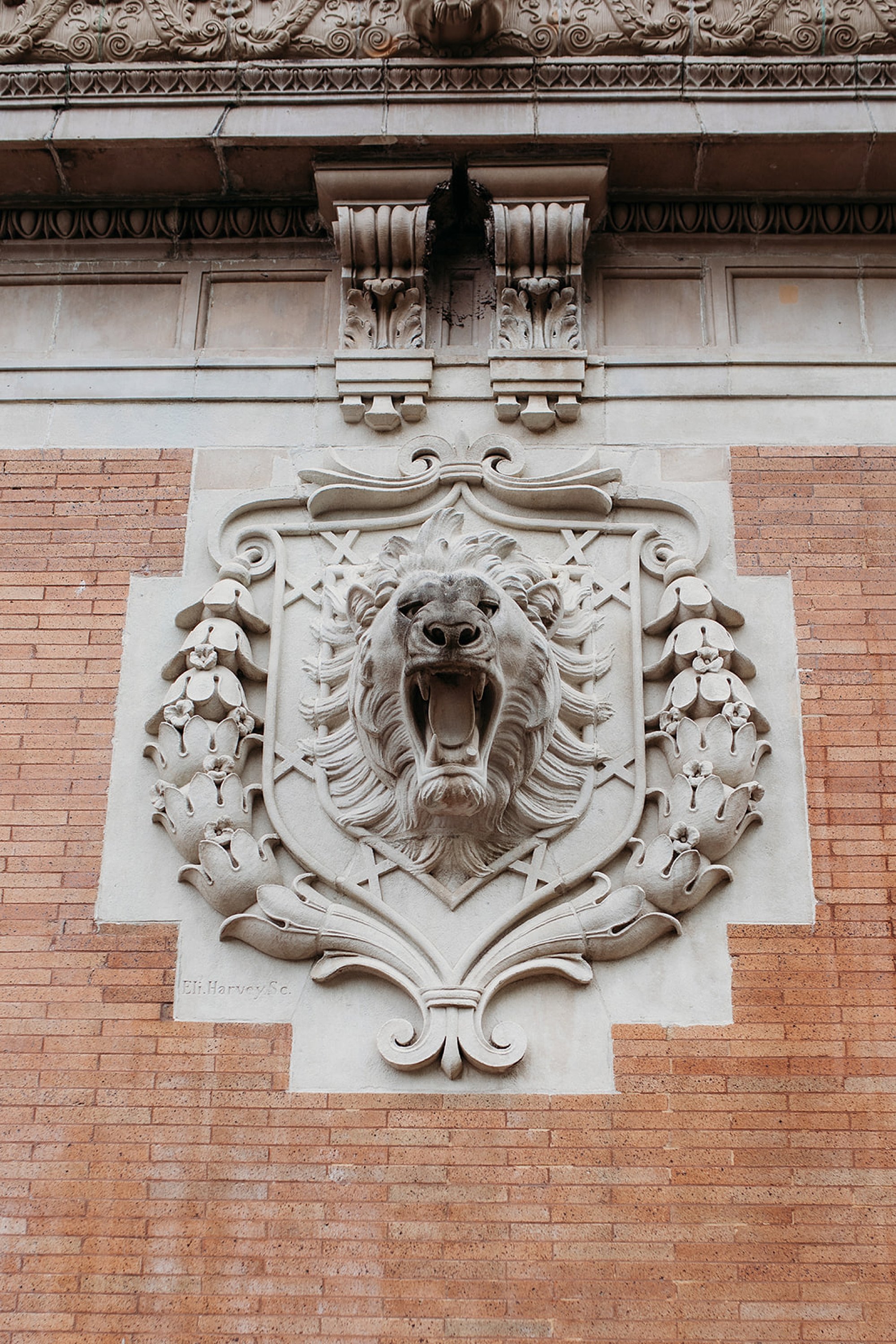 Lion roaring statue alongside brick wall of Bronx Zoo