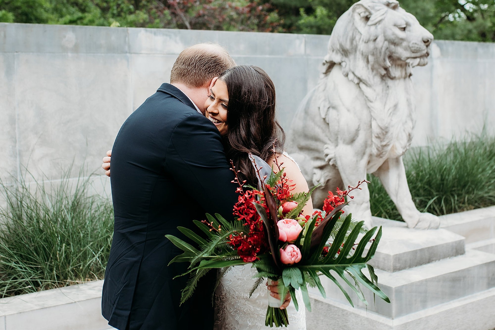 bride and groom hug near lion statue at Bronx Zoo