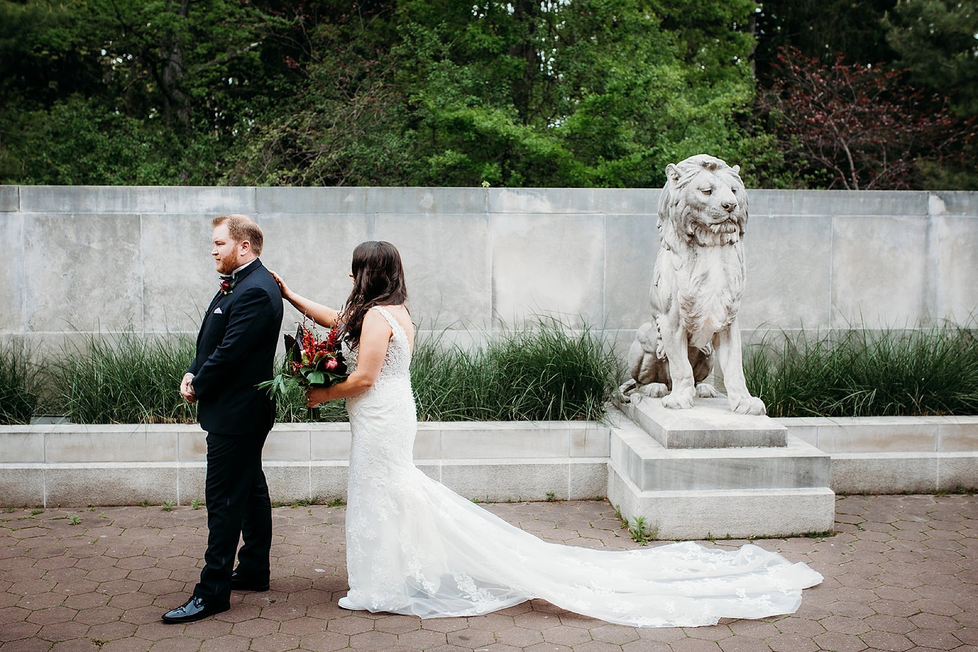 bride reaches for groom's shoulder to tap during first look in gardens of the Bronx Zoo