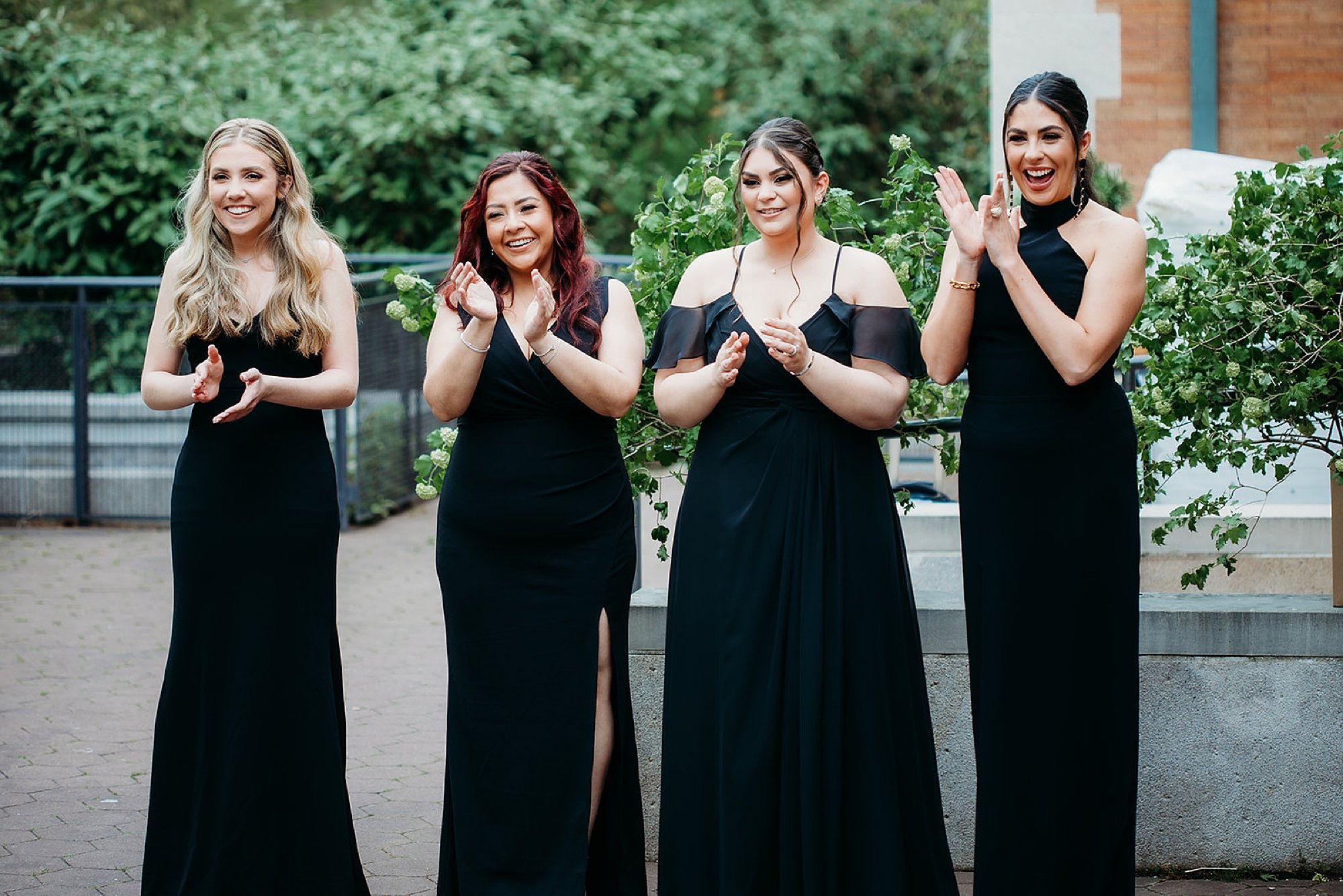 bridesmaids in black dresses clap and cheer during first look