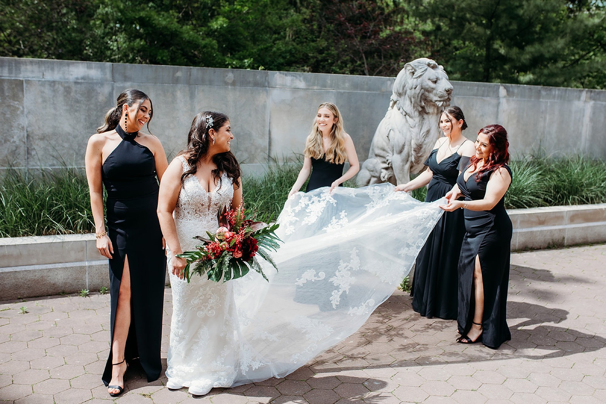 bridesmaids in black dresses help bride fluff dress and veil before first look