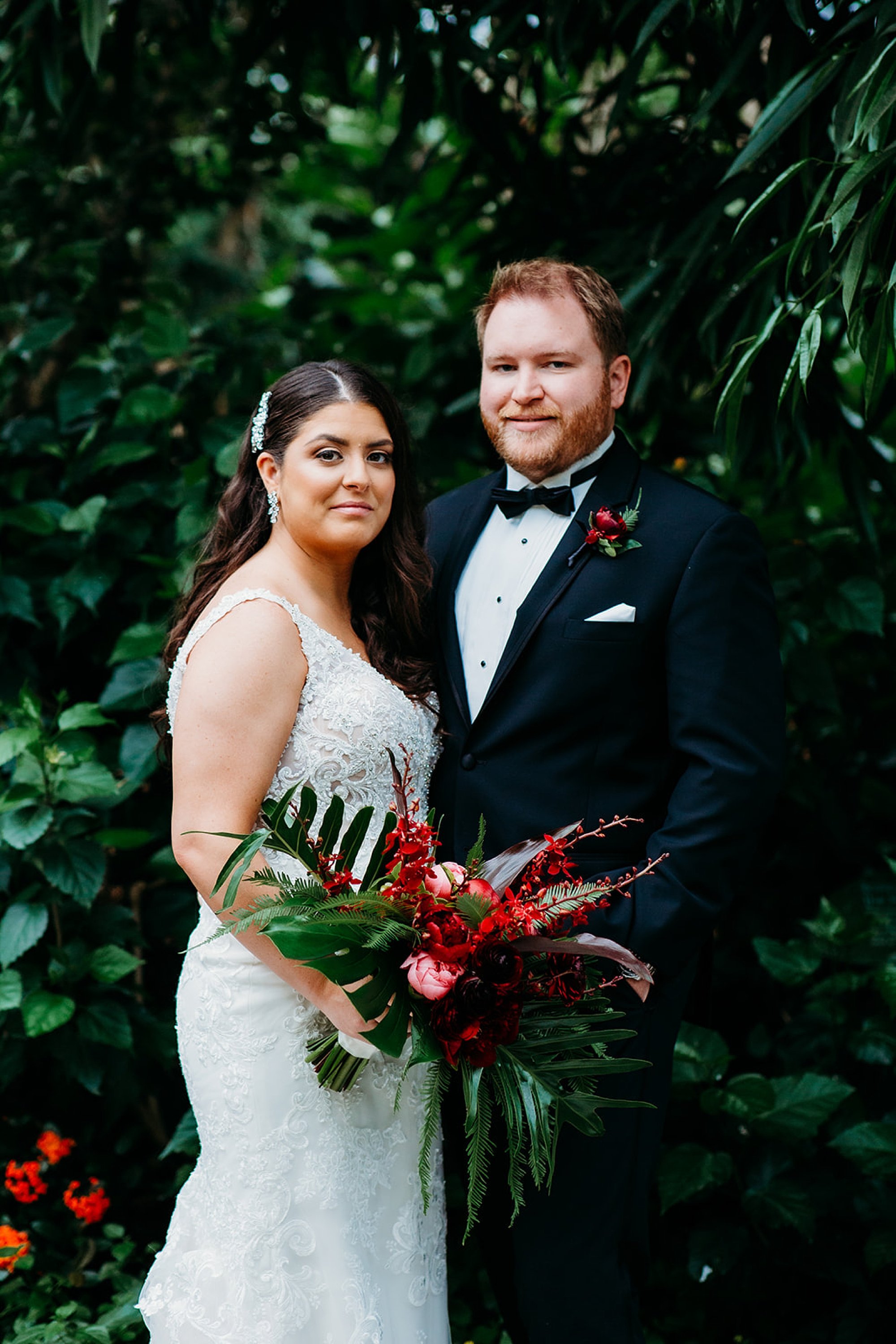newlyweds pose in Butterfly House at the Bronx Zoo while bride holds bouquet of pink tropical flowers 