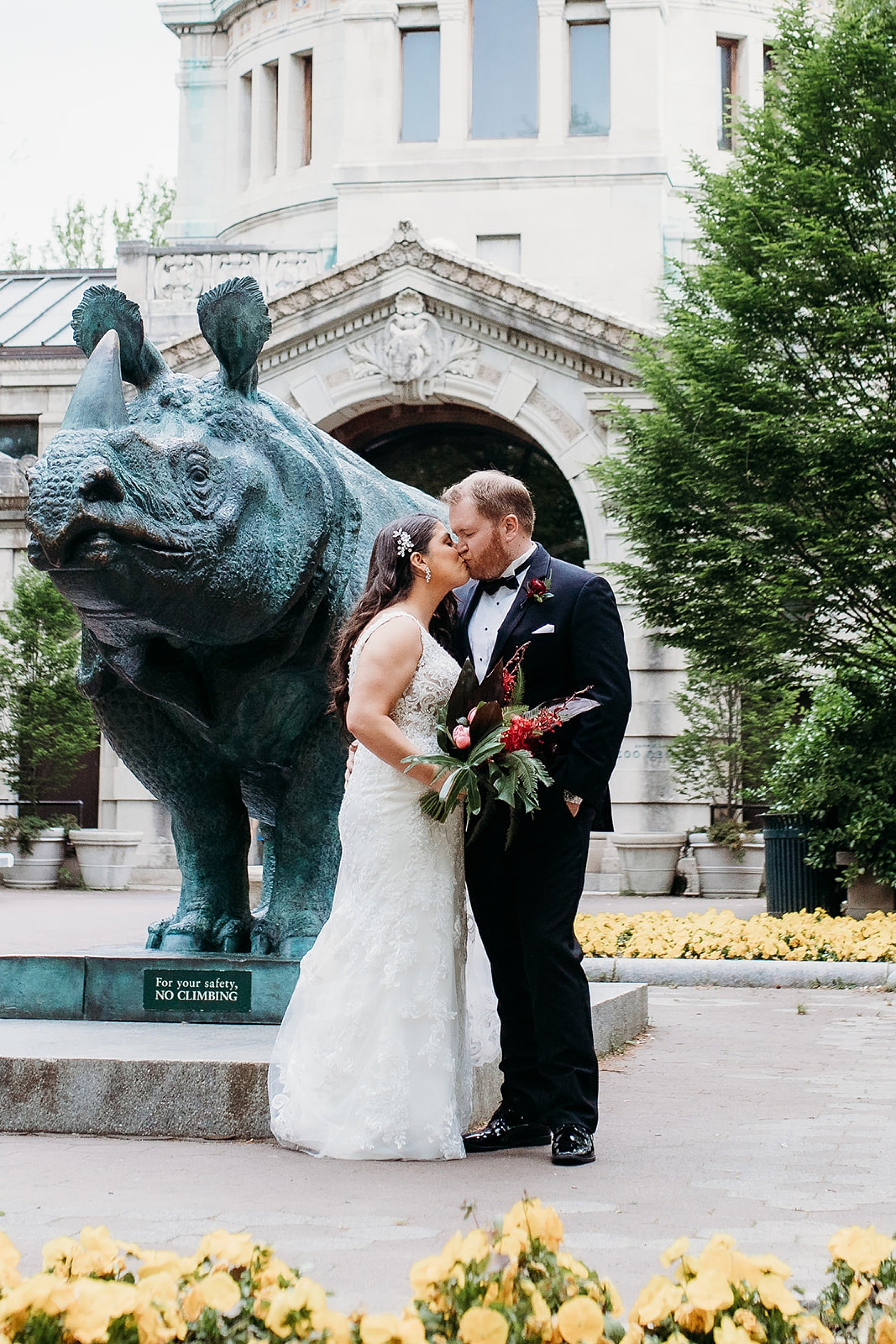 newlyweds kiss by statue of hippo at the Bronx Zoo