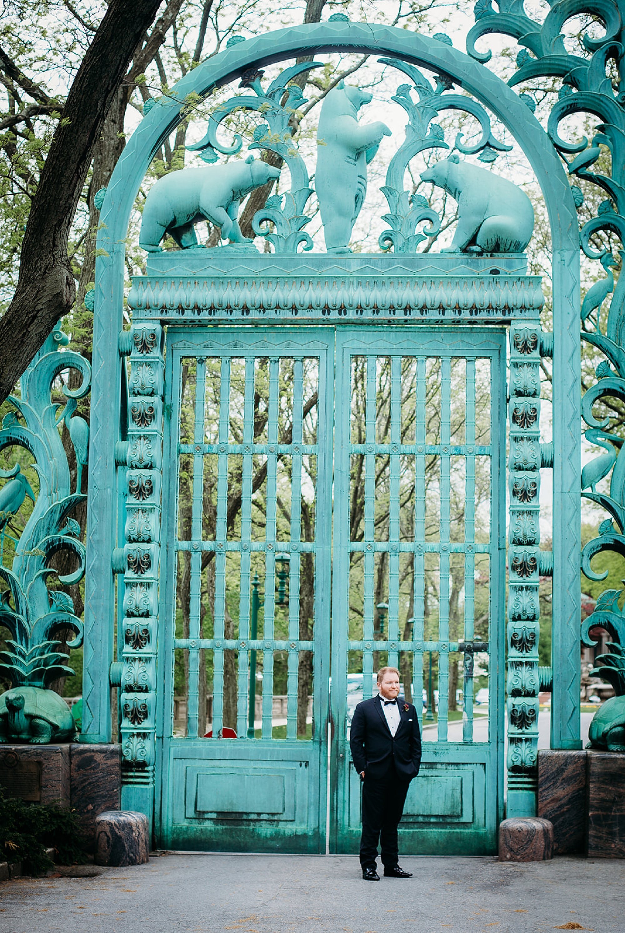 groom stands in black suit with hands in pockets beside Rainey Memorial Garden at the Bronx Zoo