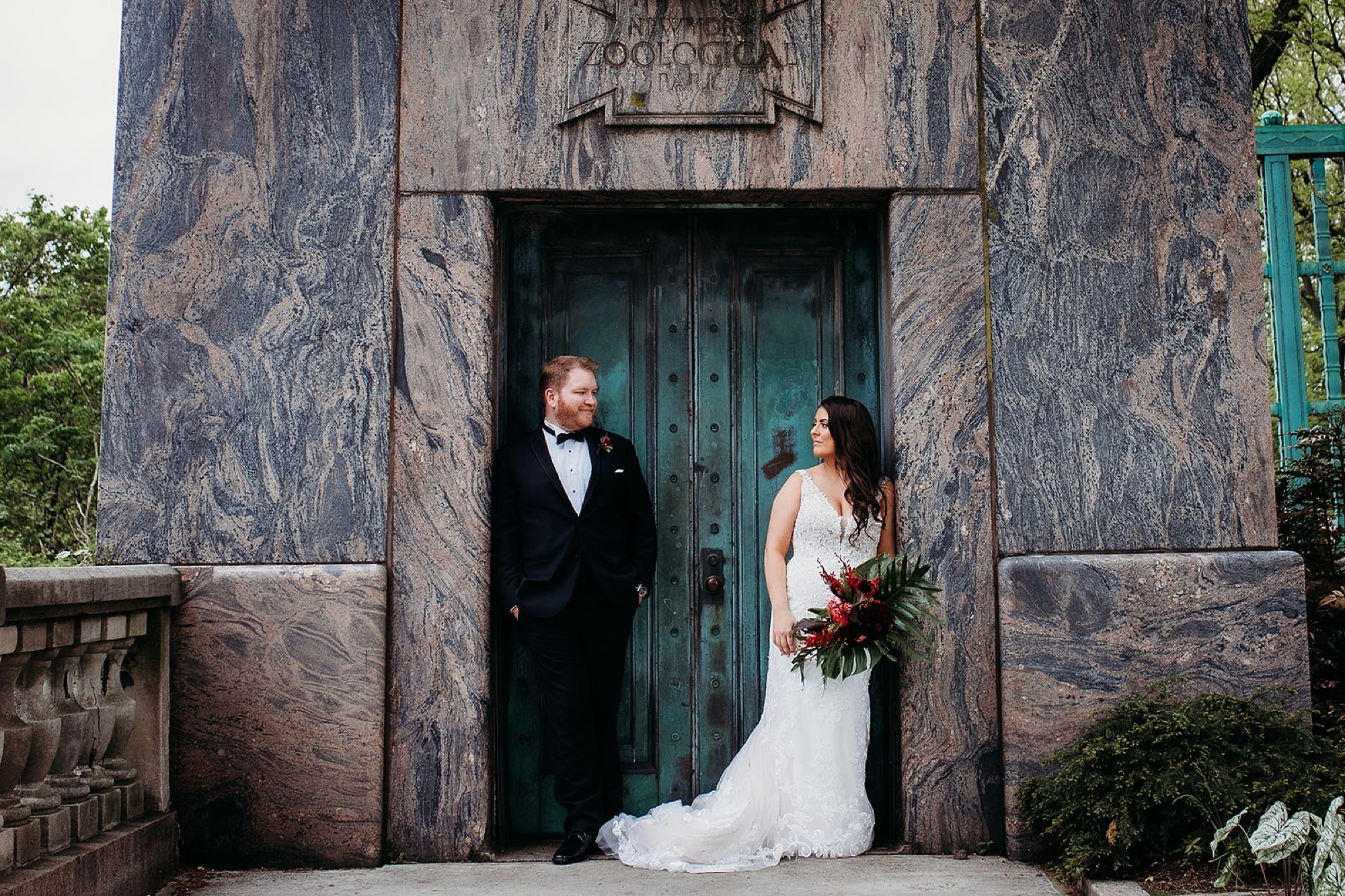 bride and groom lean on sides of brown walls at the Bronx Zoo