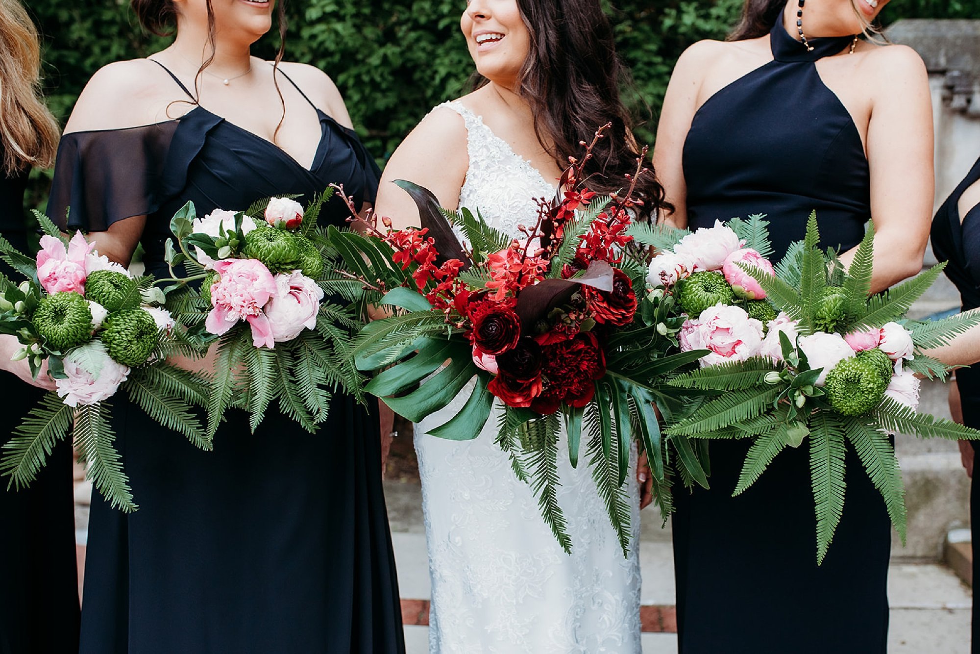 bride laughs with bridesmaids in black dresses with pink tropical bouquets