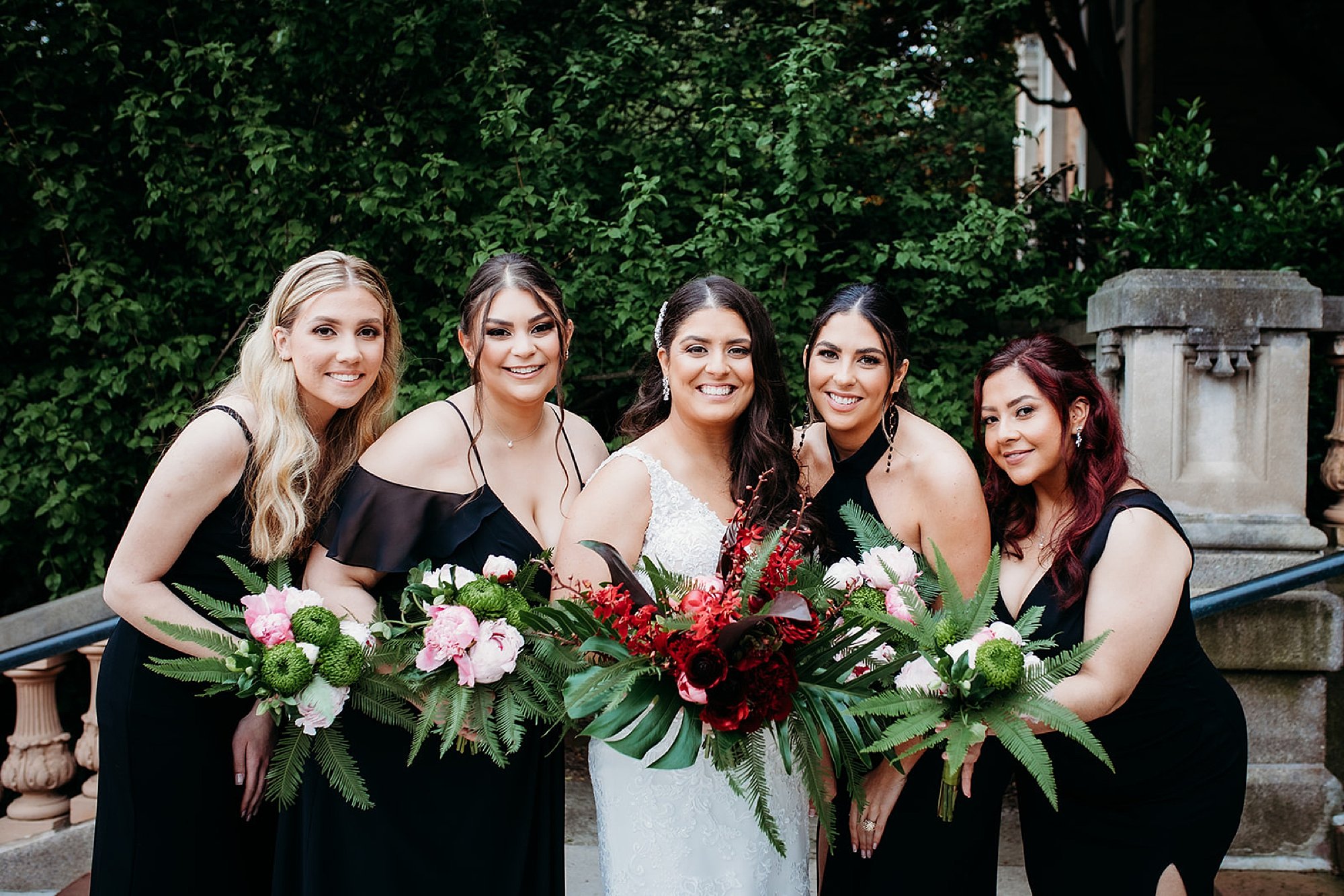 bride laughs with bridesmaids in black gowns with tropical bouquets 