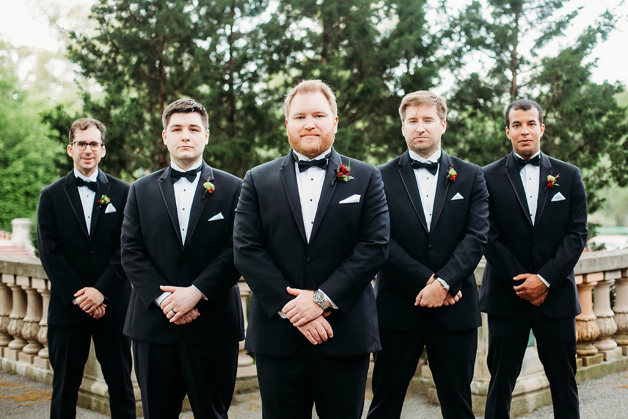 groom stands with groomsmen in black suits behind him