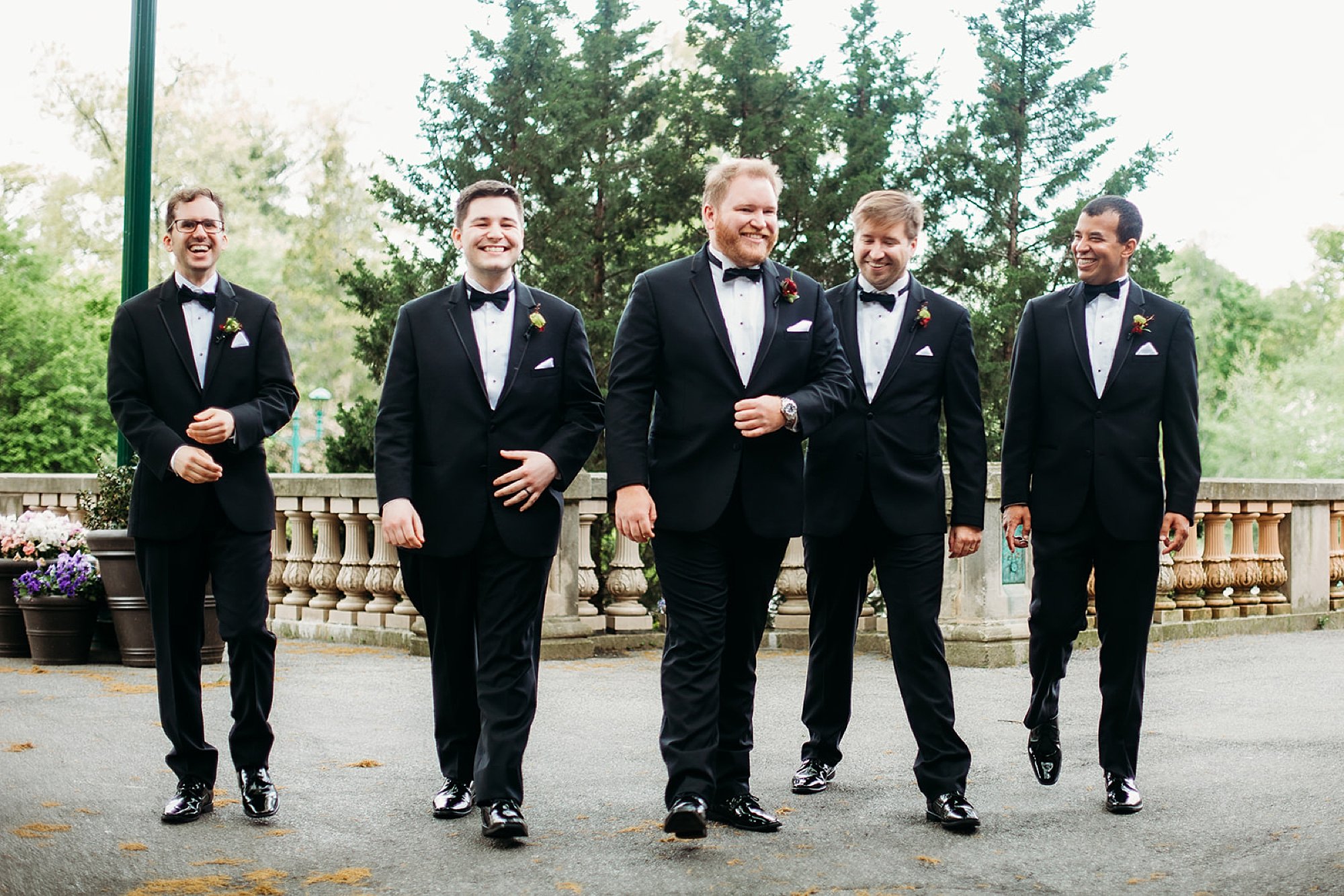 groom walks with groomsmen on stone bridge at the Bronx Zoo