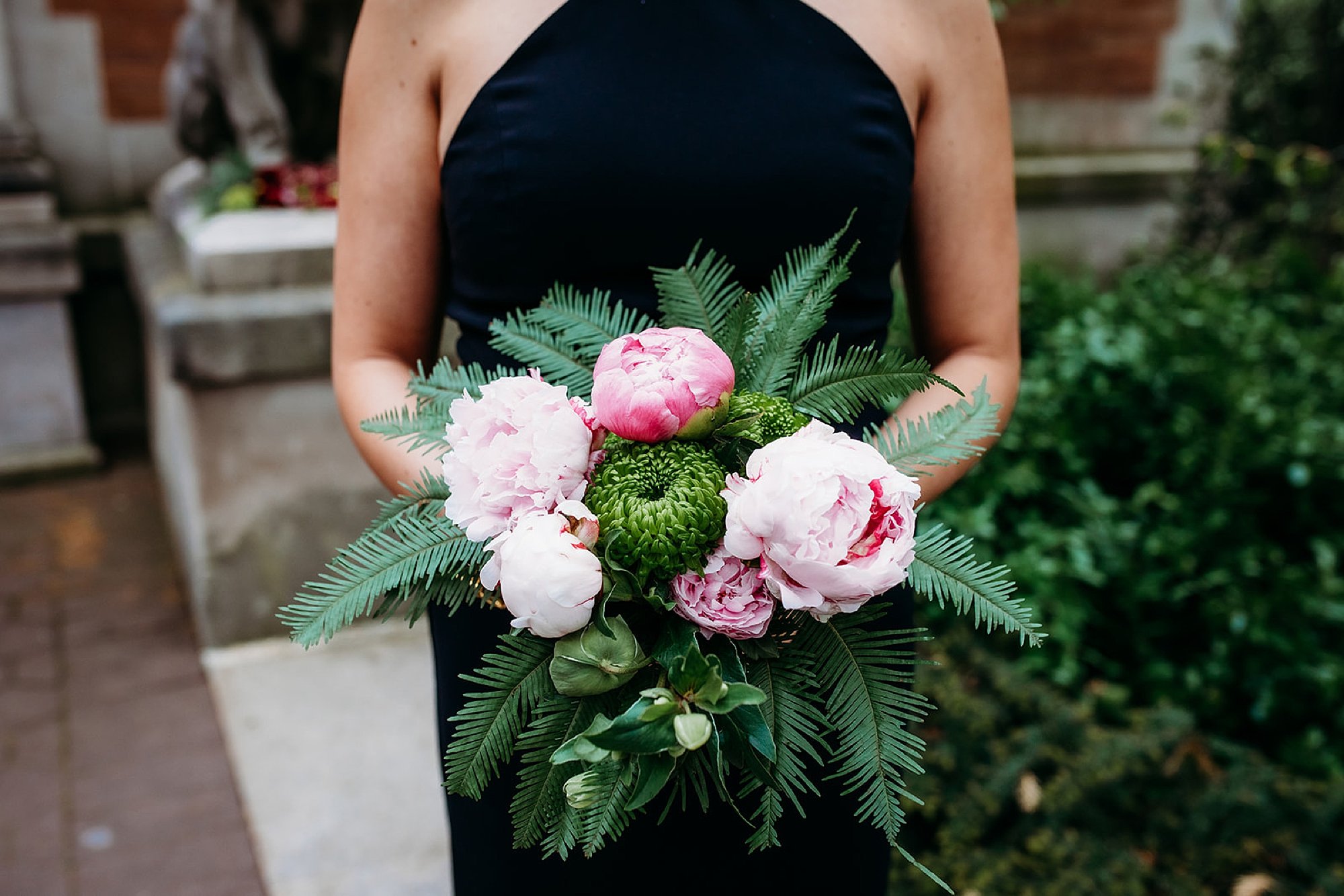 bridesmaid in black dress holds bouquet with pink tropical flower