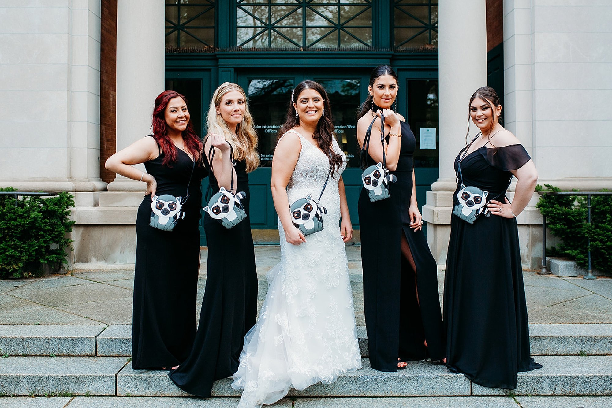 bride poses with bridesmaids holding lemur purse on steps at the Bronx Zoo