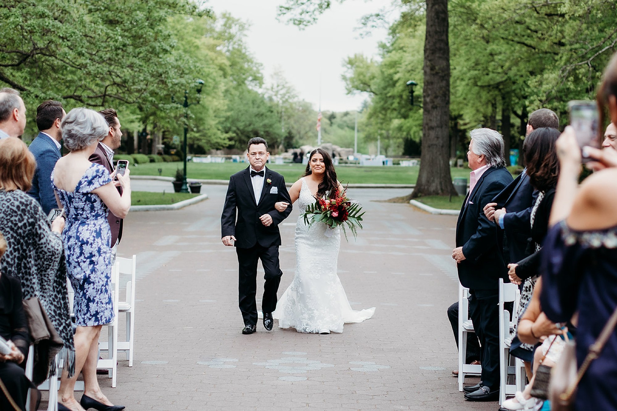 bride walks down aisle with father for wedding ceremony outside the Elephant House at the Bronx Zoo