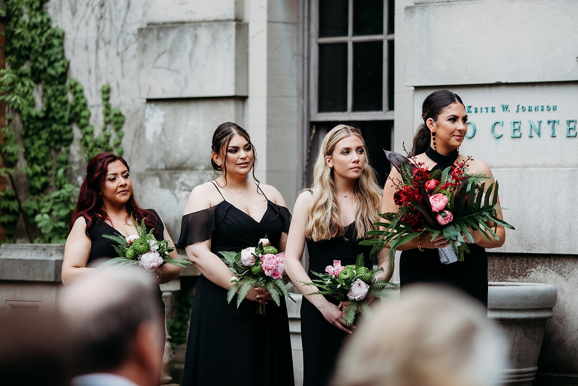 bridesmaids in black dresses hold tropical bouquets watching ceremony 