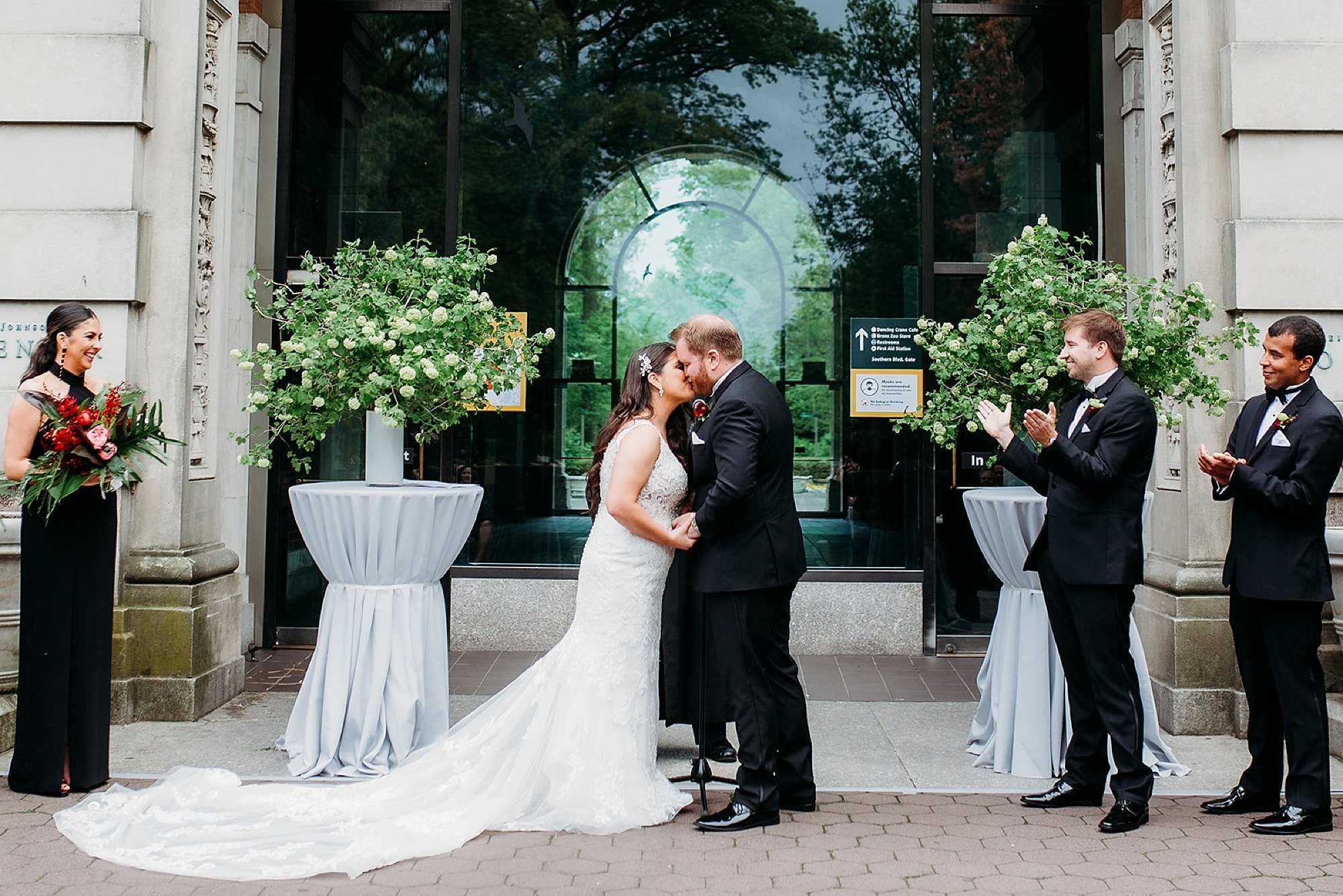 bride and groom kiss holding hands during wedding ceremony outside the Elephant House at the Bronx Zoo
