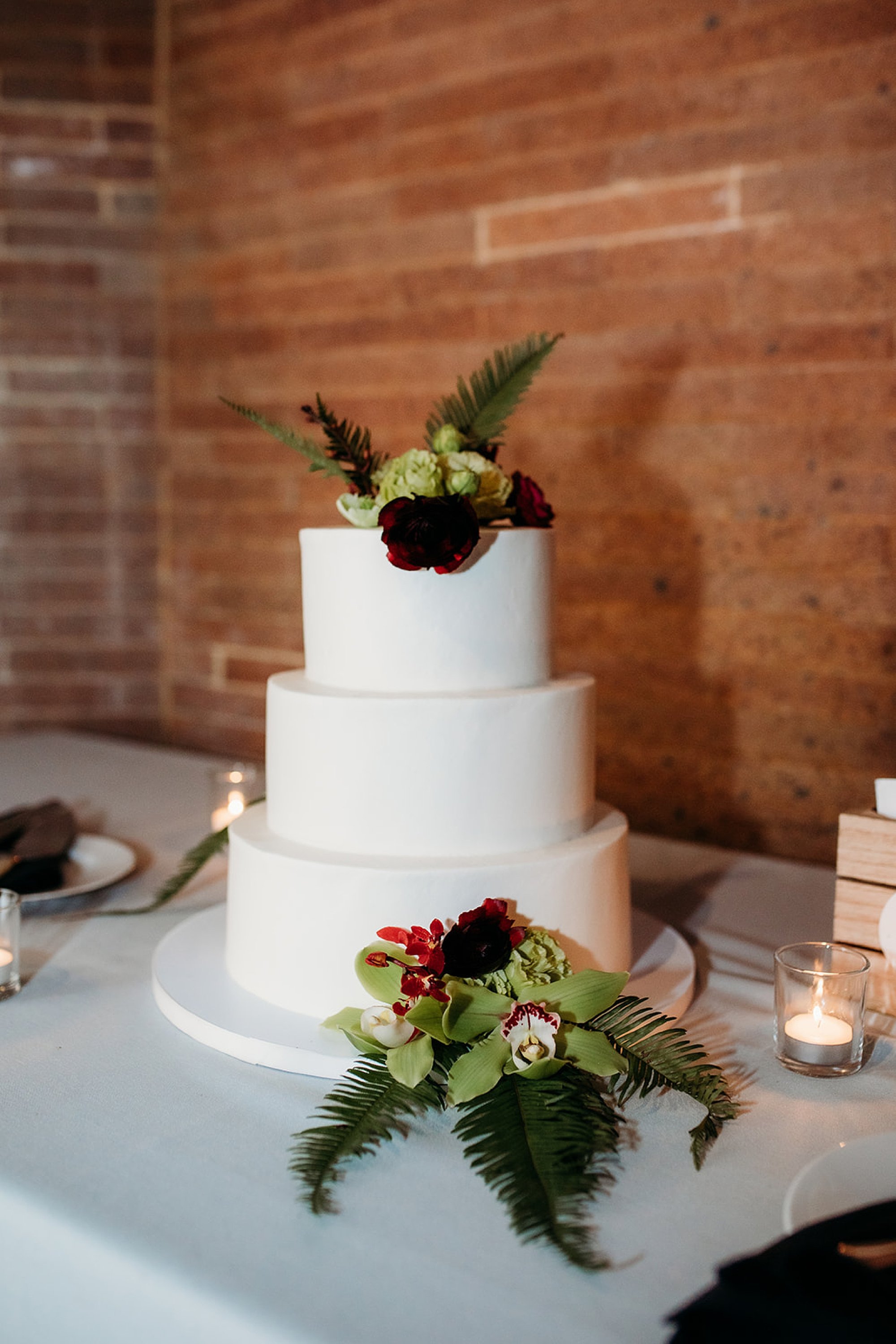 tiered wedding cake with green and red flowers at The Bronx Zoo wedding reception at the Old Lion House