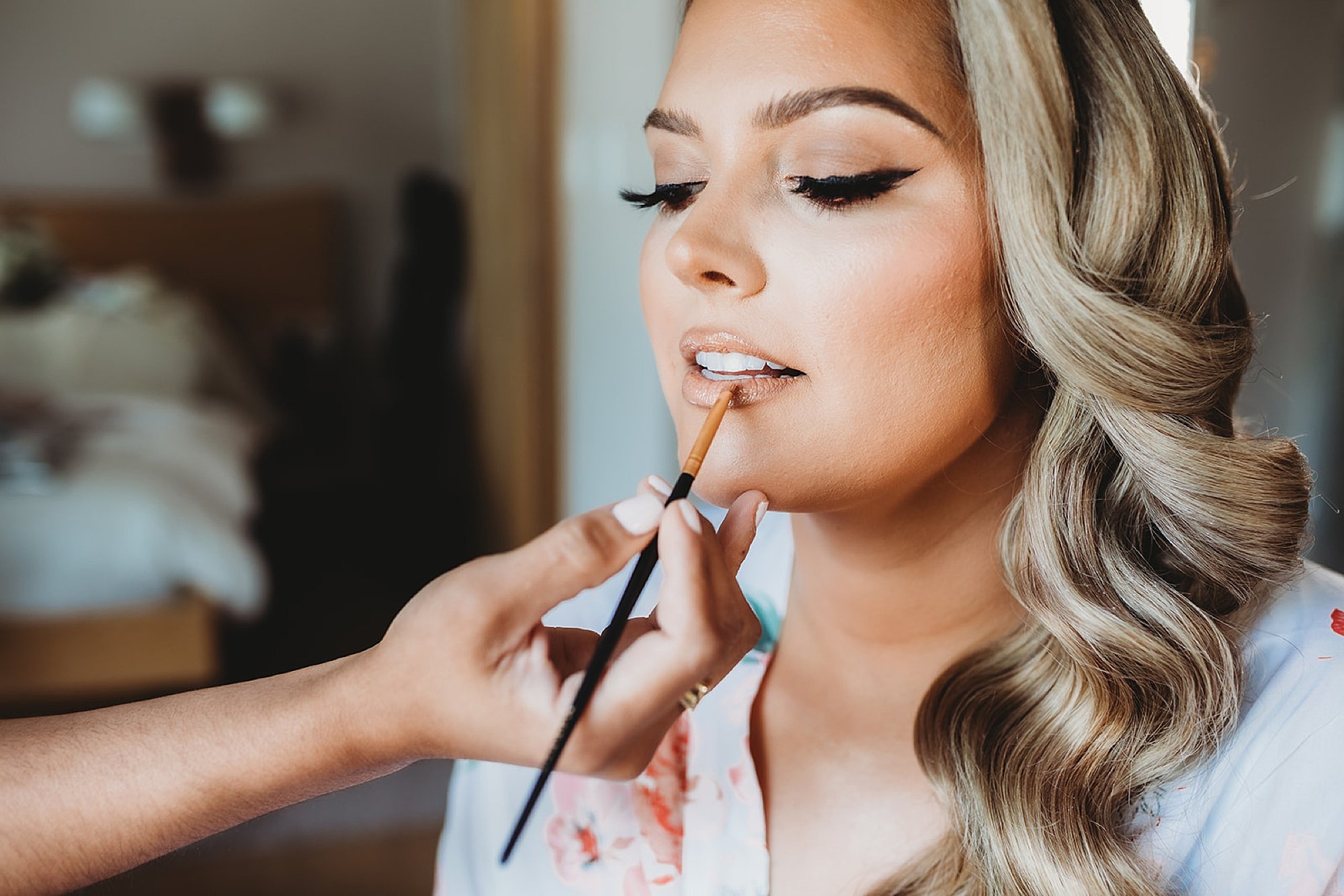 blonde woman looks down while makeup artist applies lip gloss