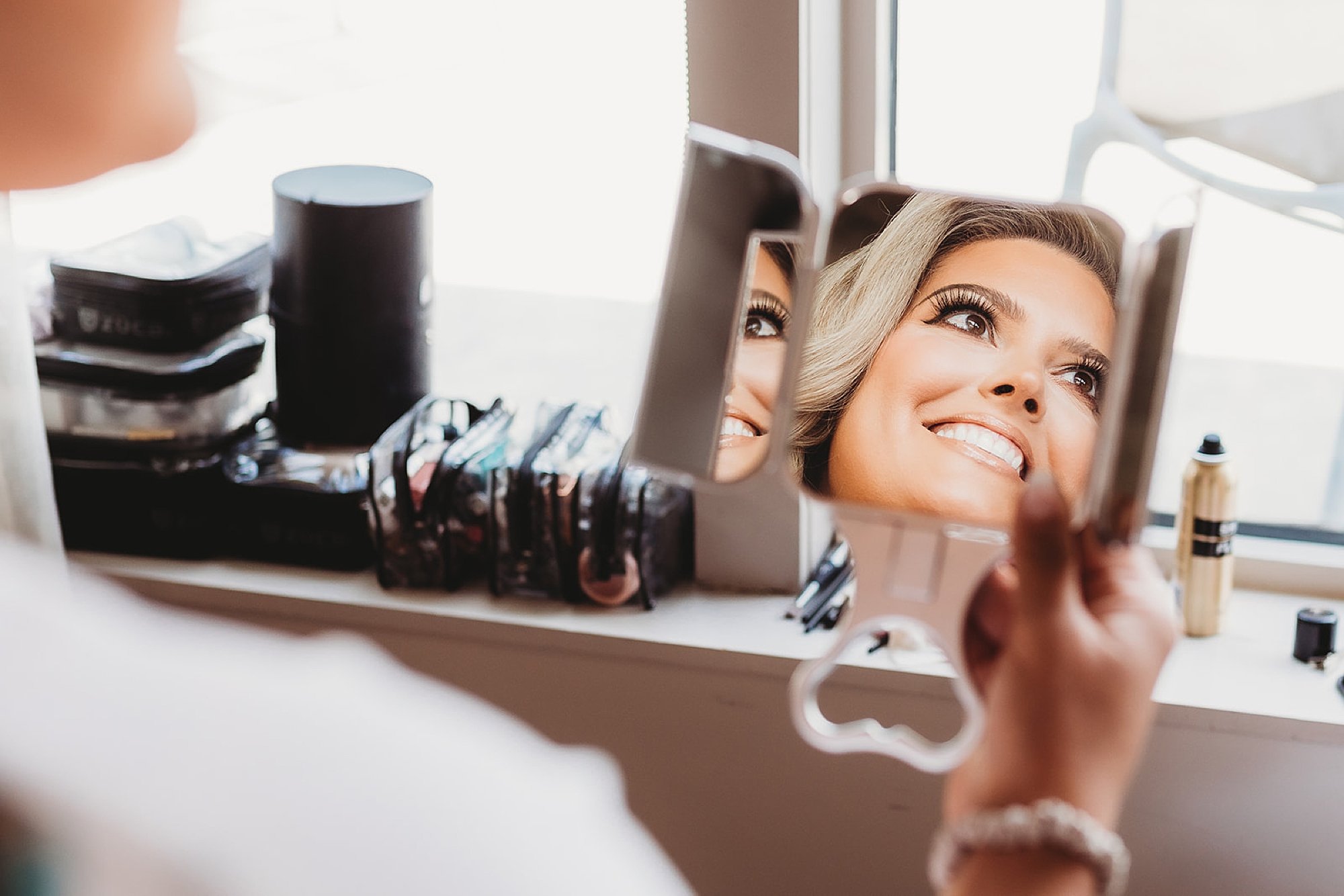 bride smiles in mirror during makeup application 