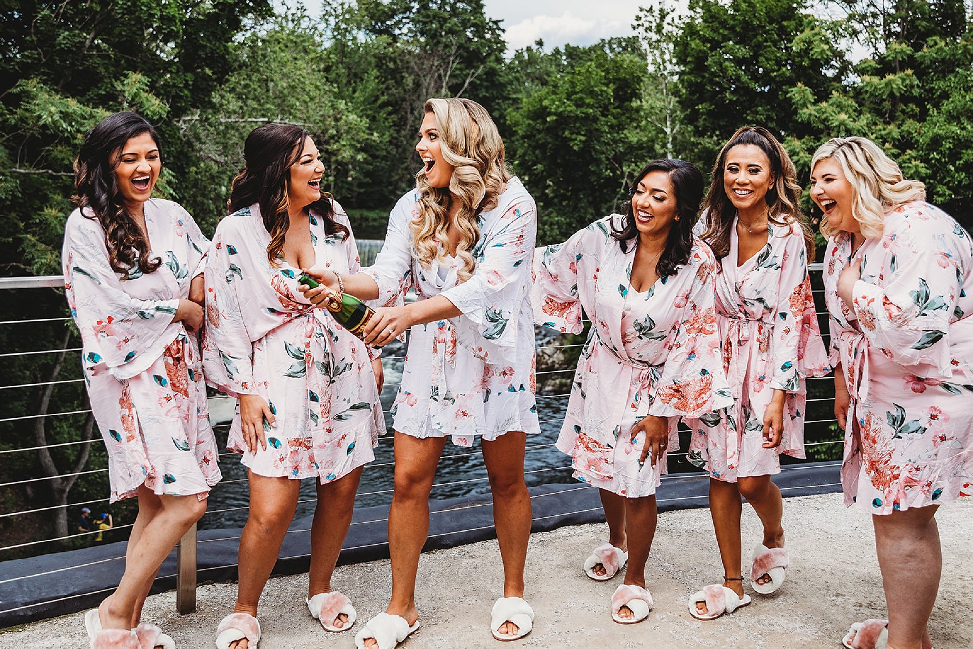bride pops bottle of champagne with bridesmaids on balcony at the Roundhouse in matching floral pajamas 