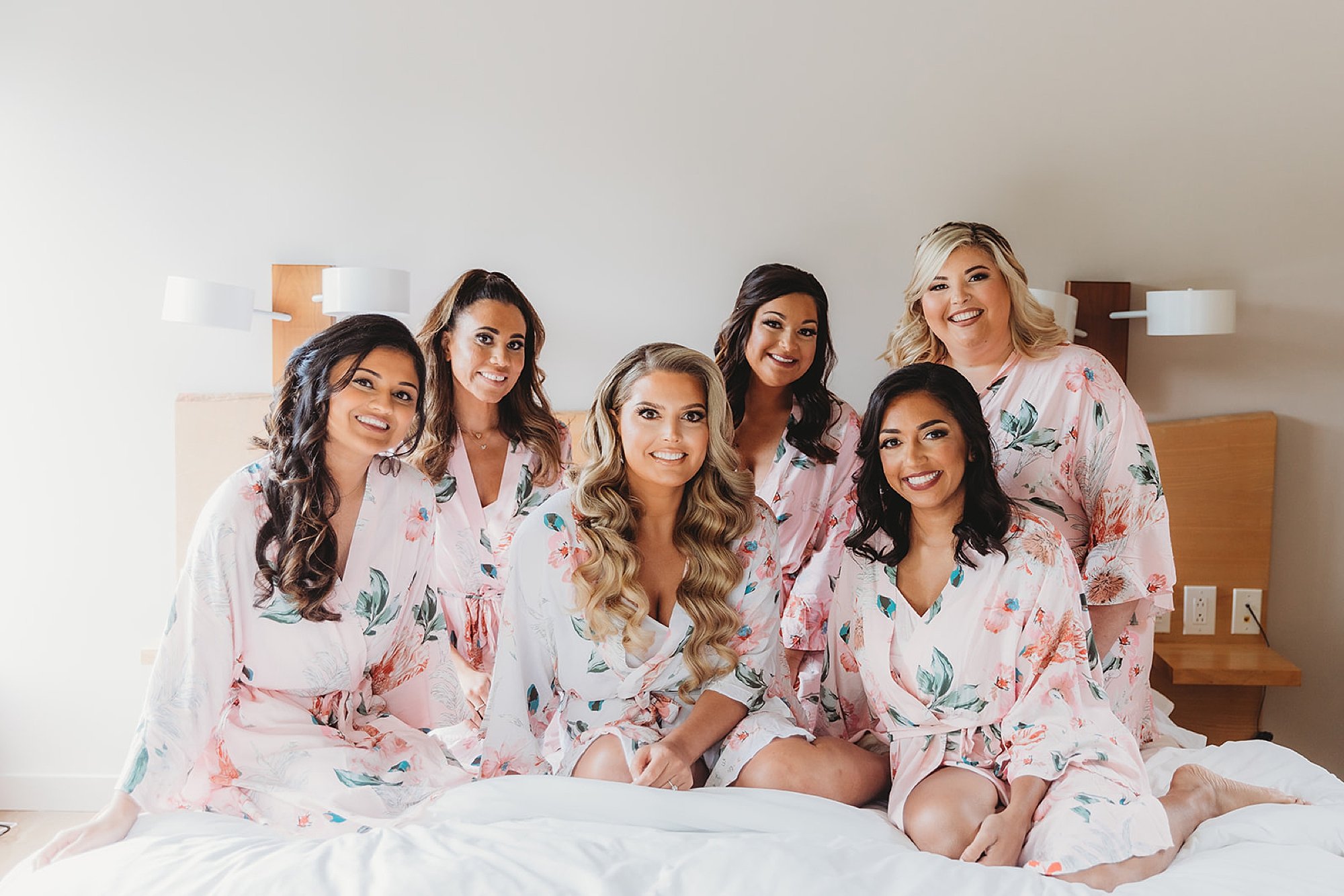 bridesmaids sit with bride on bed at the Roadhouse in matching floral robes