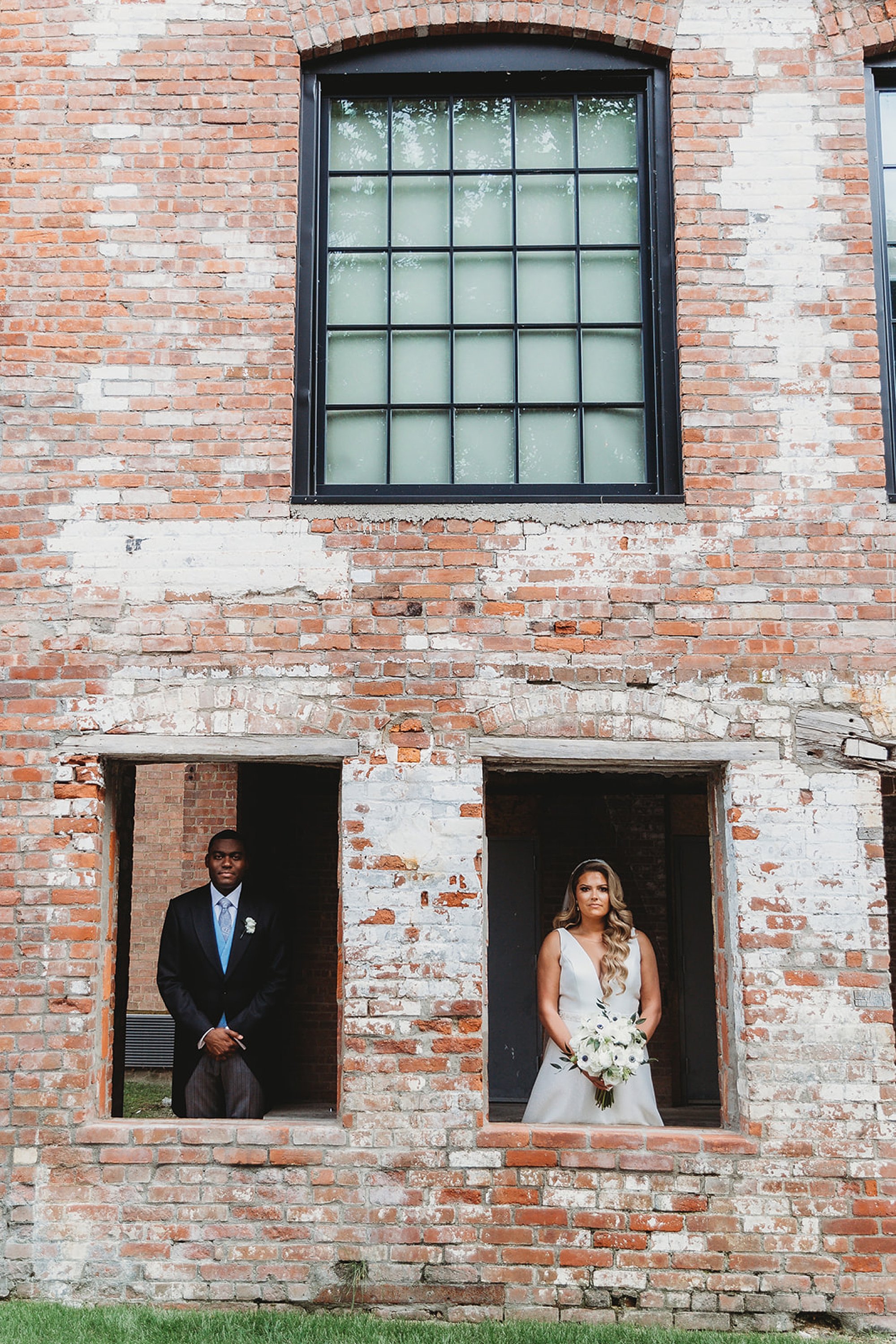 bride and groom pose in windows of brick building at The Roadhouse