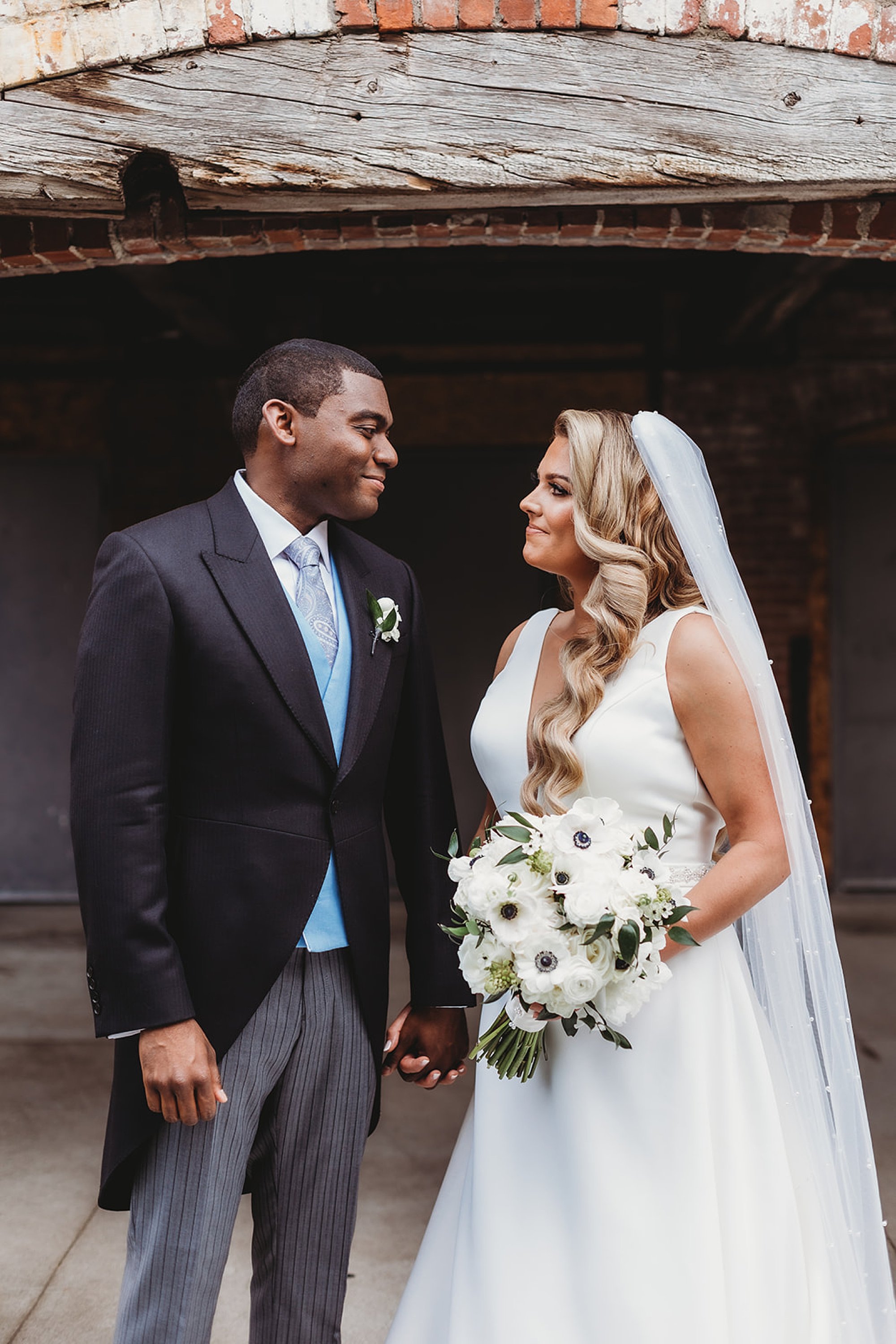bride and groom smile at each other during portraits near brick building 