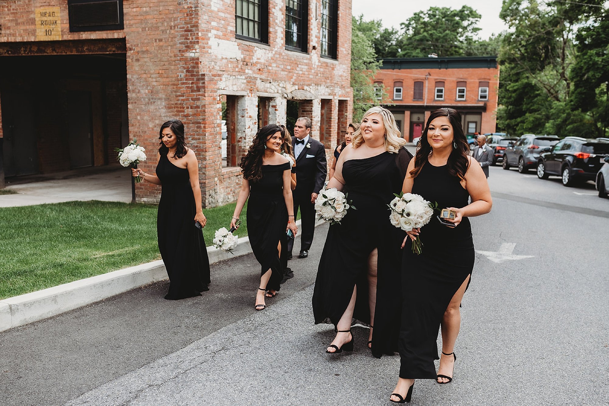 bridesmaids in black gowns walk near brick building at The Roadhouse
