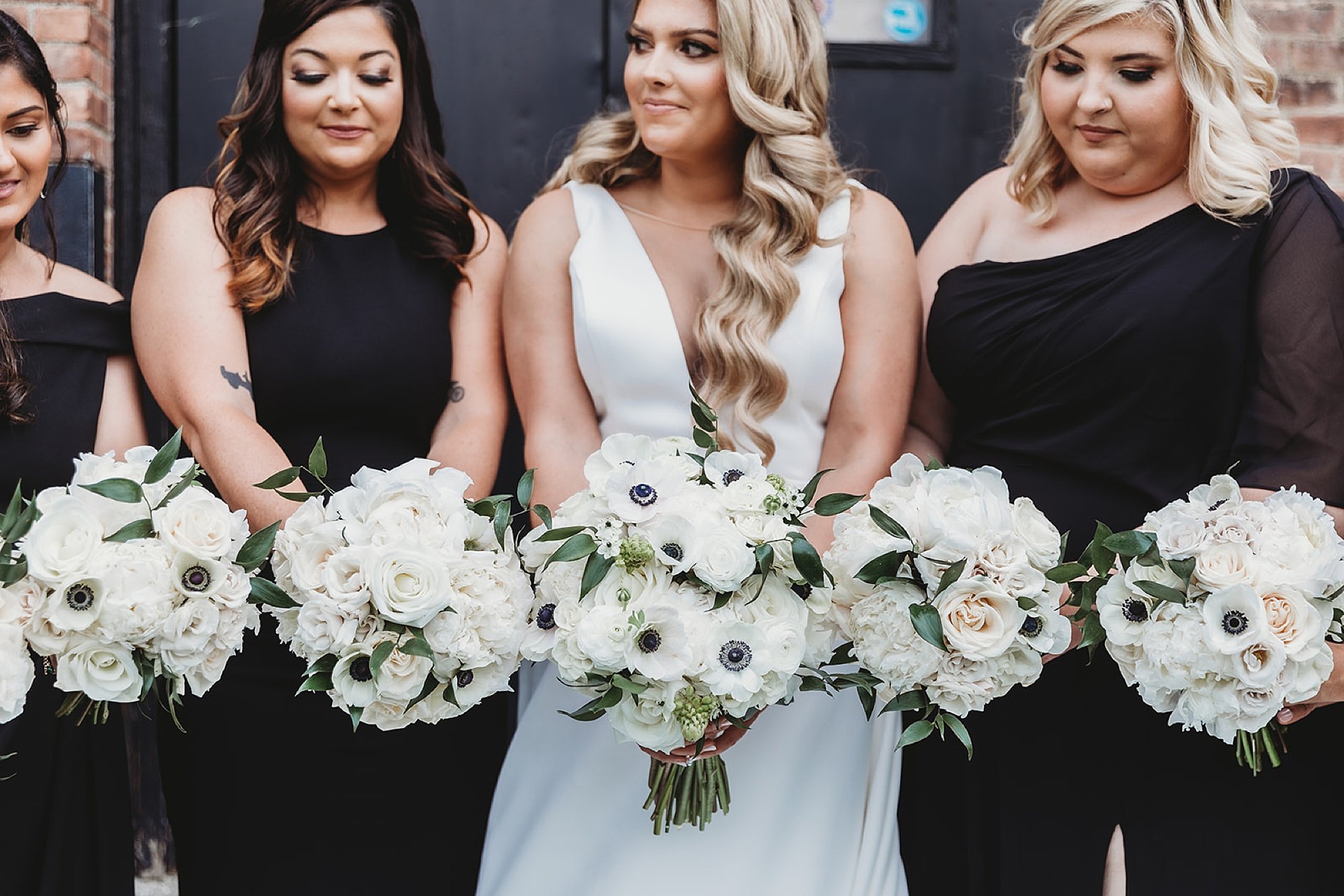 bride and bridesmaids in mismatched black gowns hold bouquets of white flowers 