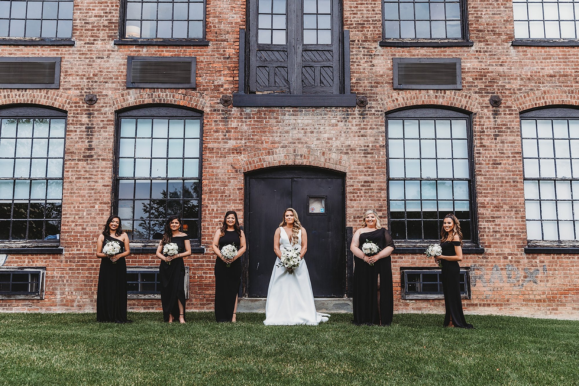 bride stands with bridesmaids in front of brick building 