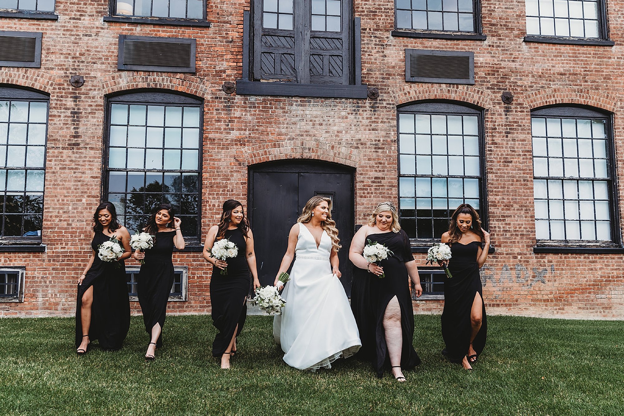 bride walks with bridesmaids in black gowns outside brick building at The Roadhouse in Beacon NY