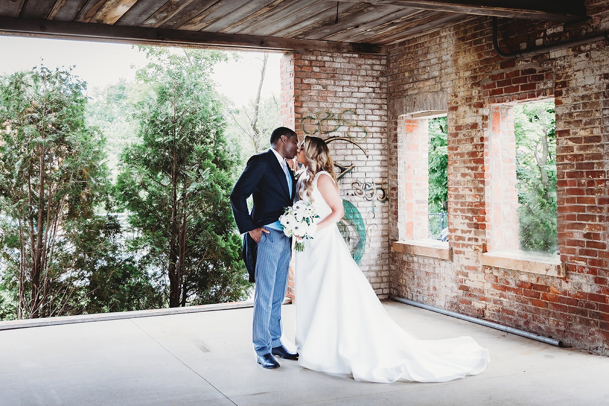 bride and groom kiss in corner of room with brick walls 