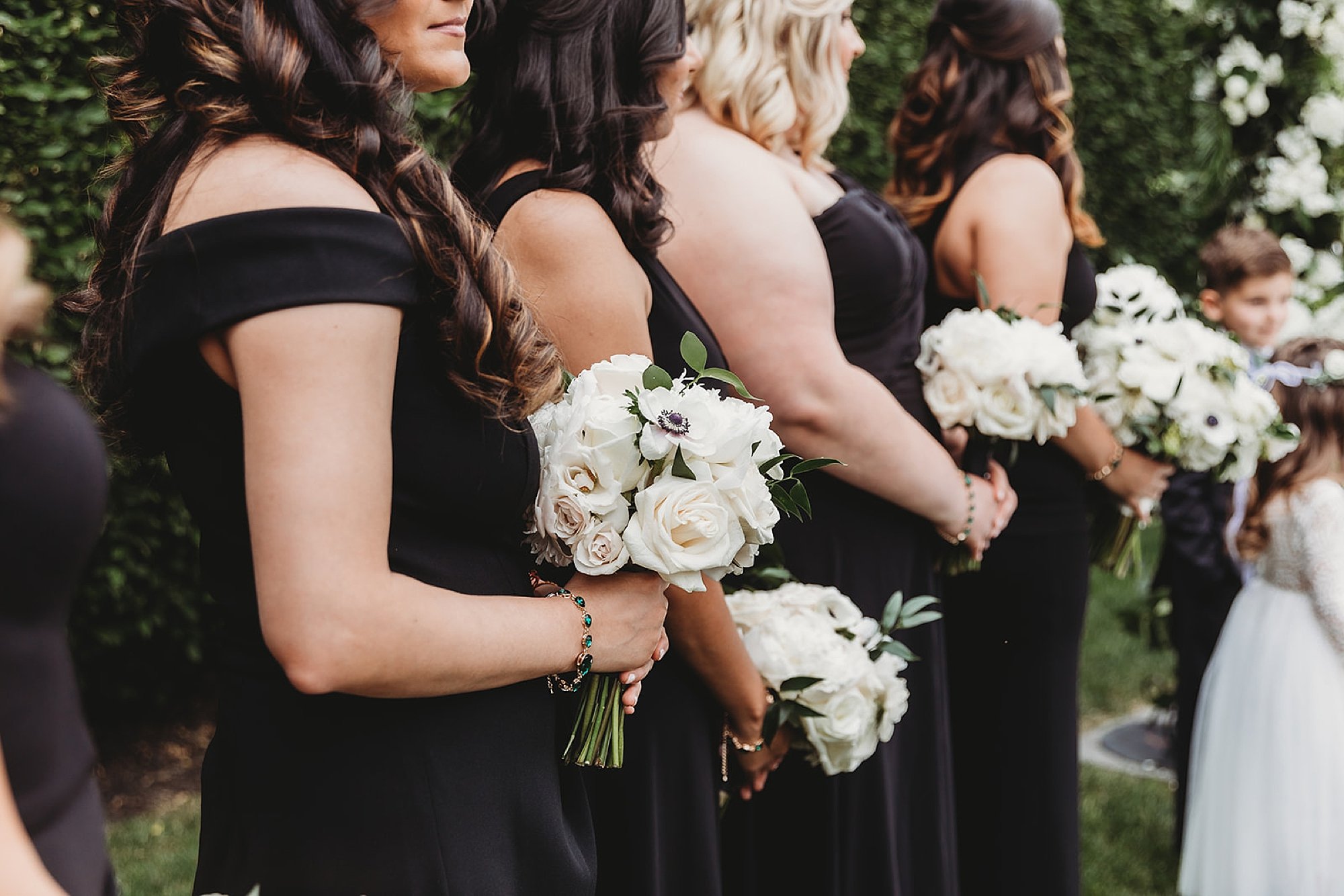 bridesmaids in black gowns hold white flowers