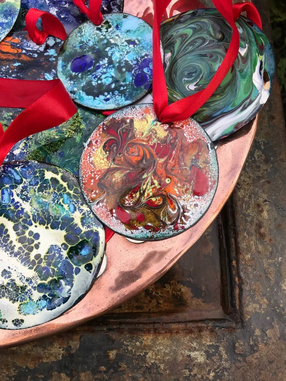 Colorful, abstract glass ornaments with red ribbons on a pink surface.