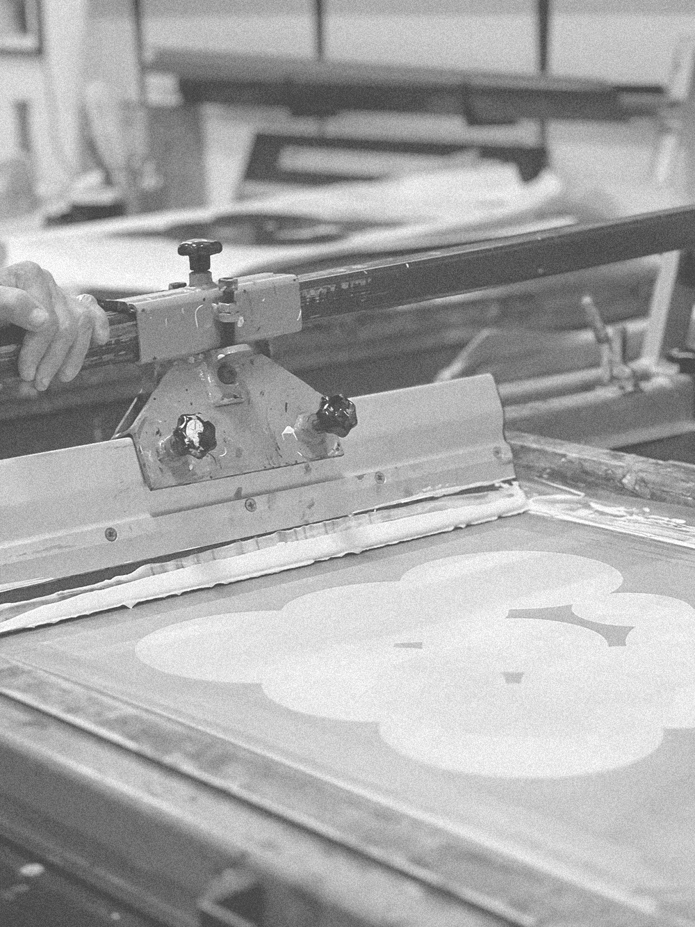 Ink and squeegee working a stencil on the print bed, in a black-and-white photo.