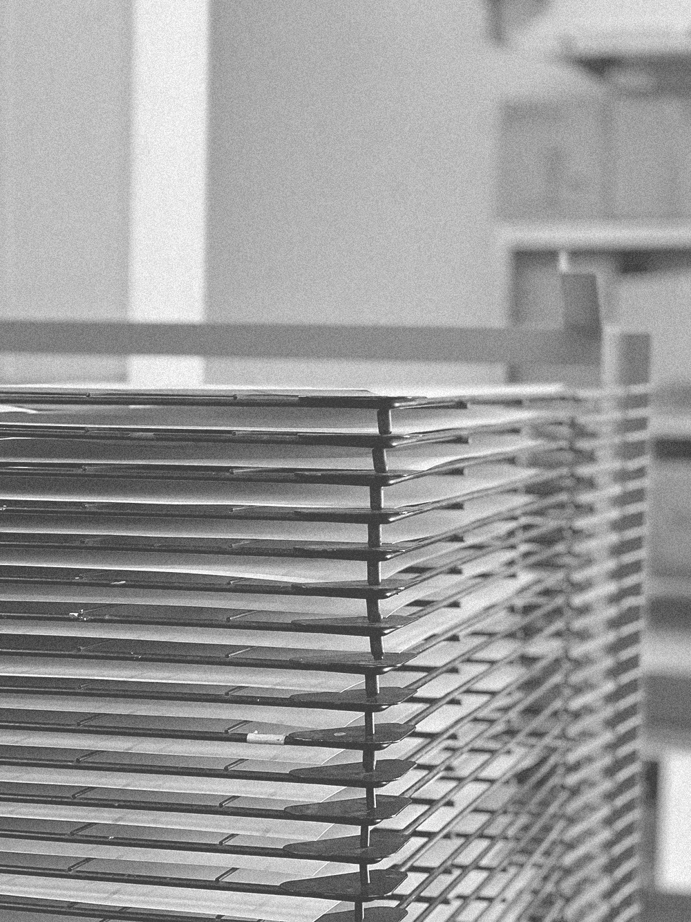 Black and white photograph of a tall metal drying rack filled with prints