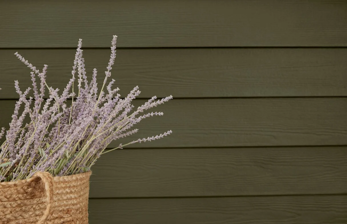 A woven basket with lavender flowers against a horizontal green wooden wall.