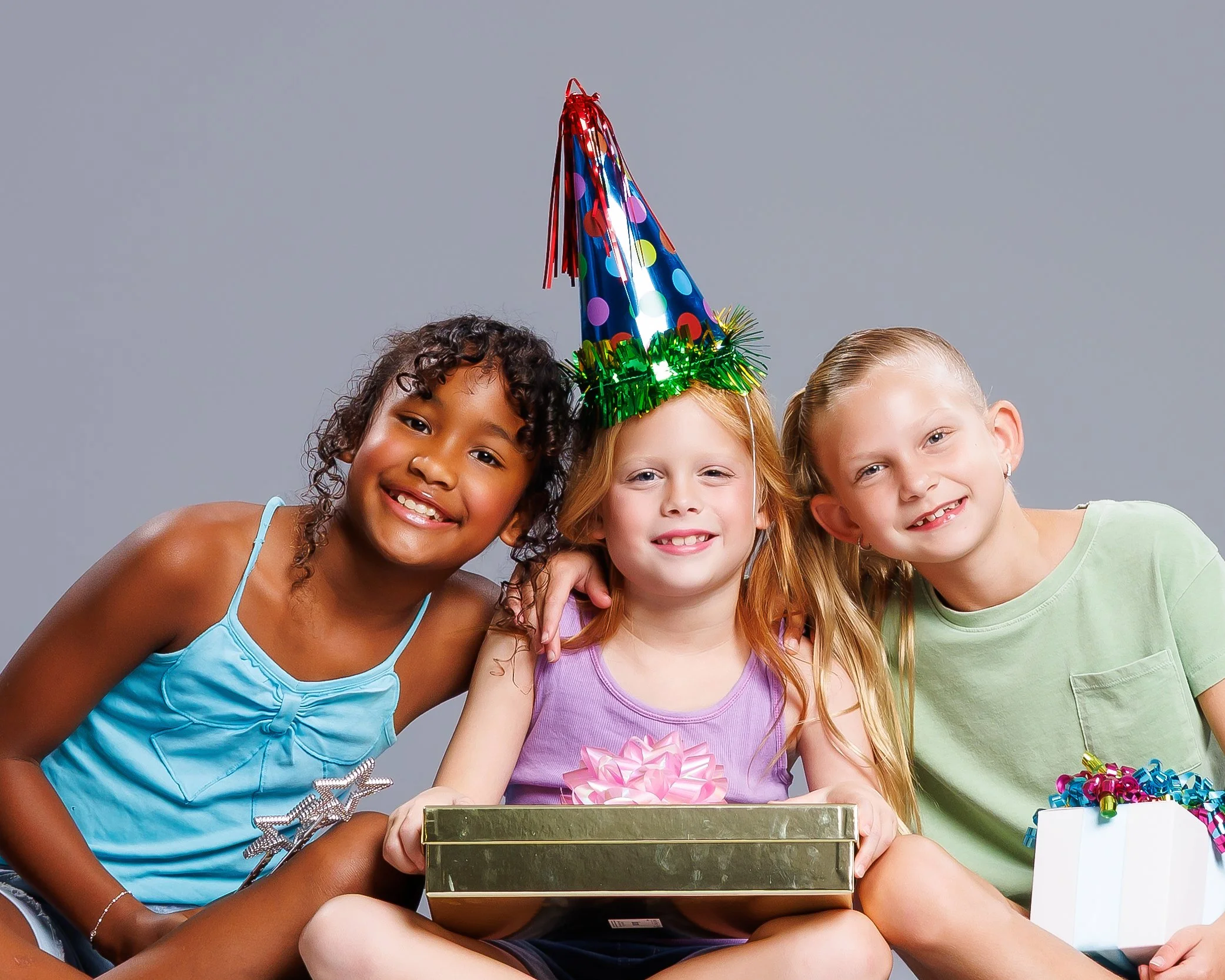 Group of children celebrating birthday party, wearing party hats, with gift box and decorations.