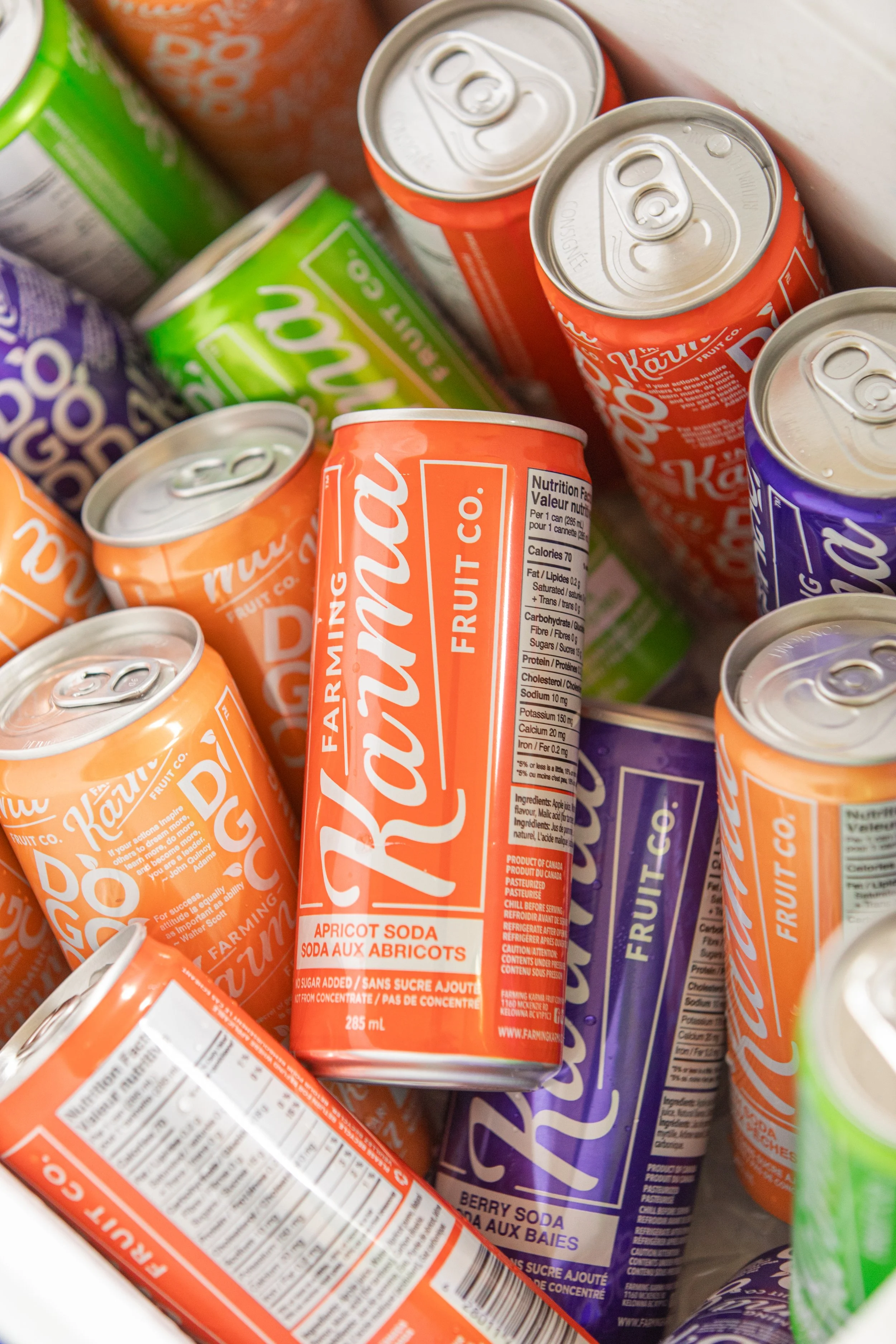 An assortment of canned sodas and fruit drinks, including cans of orange apricot soda and purple berry soda.