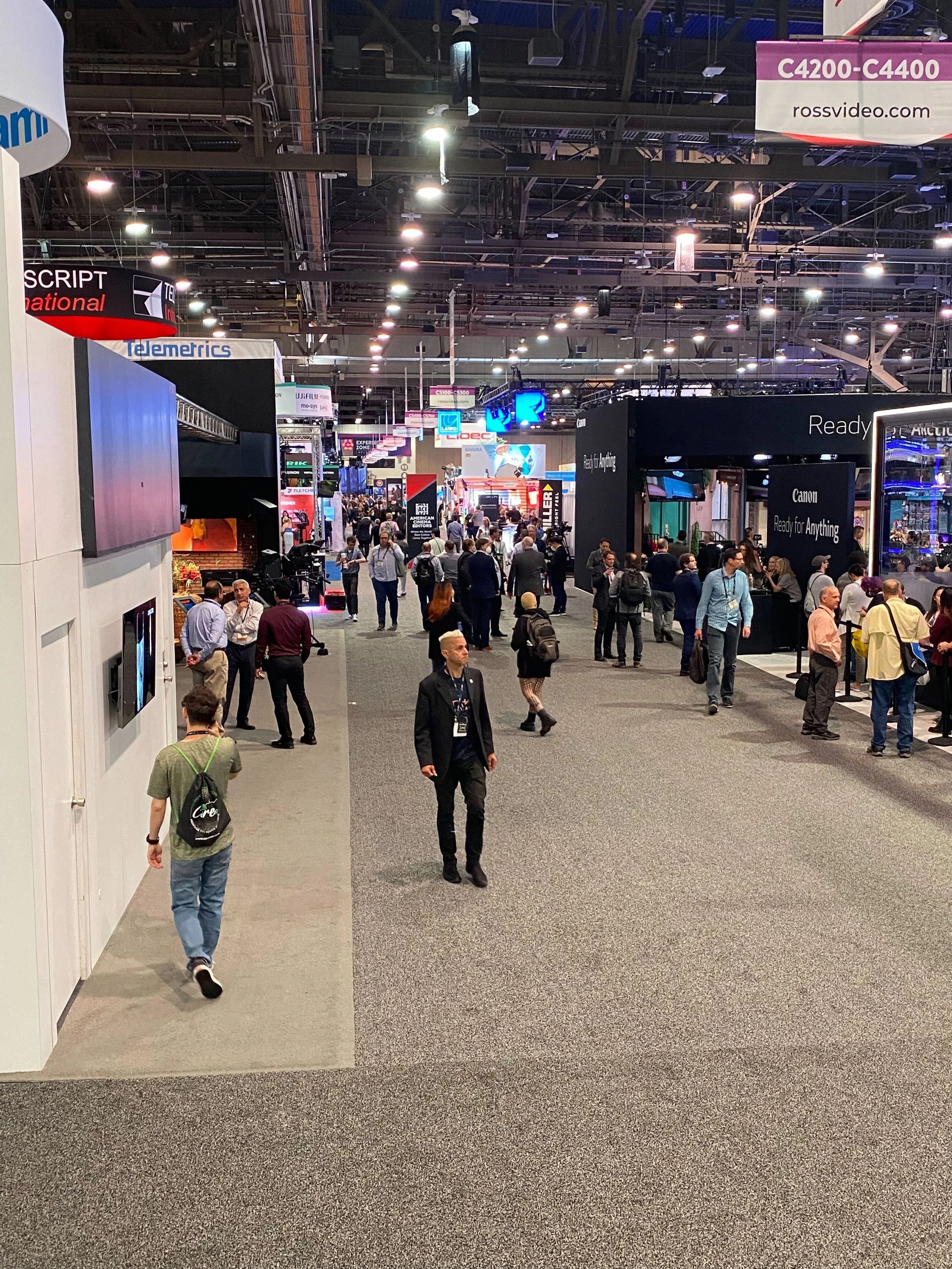 A busy trade show or convention hall with various booths and displays, and numerous attendees walking and talking.