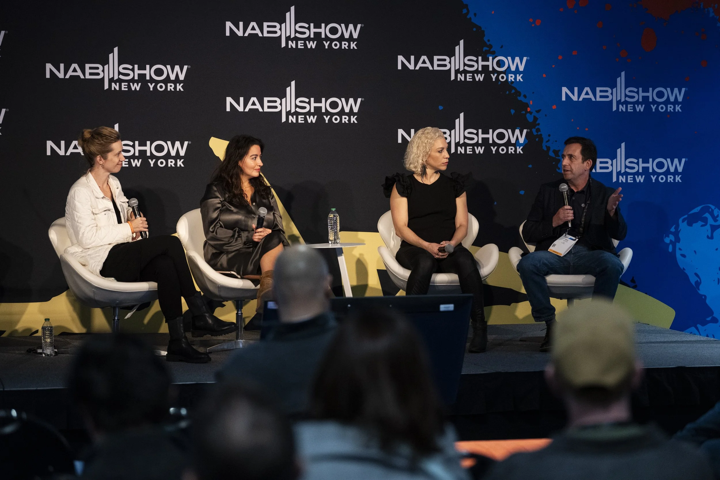 A panel discussion at NAB Show New York, with four people seated on stage holding microphones, in front of a dark backdrop with NAB Show New York logos.