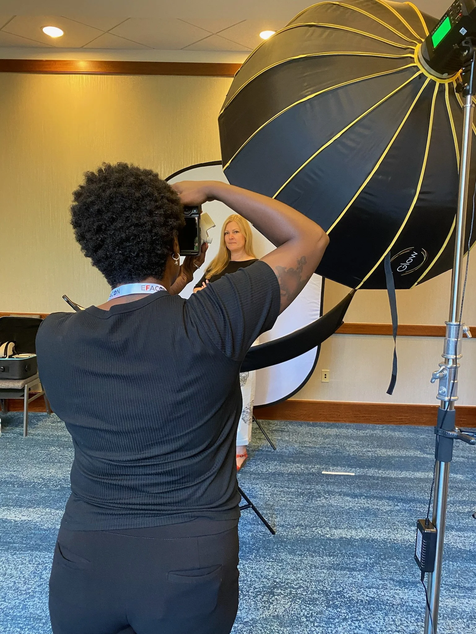 A woman with curly hair takes a photo of a blonde woman with straight hair using a camera in a photography studio with professional lighting equipment.