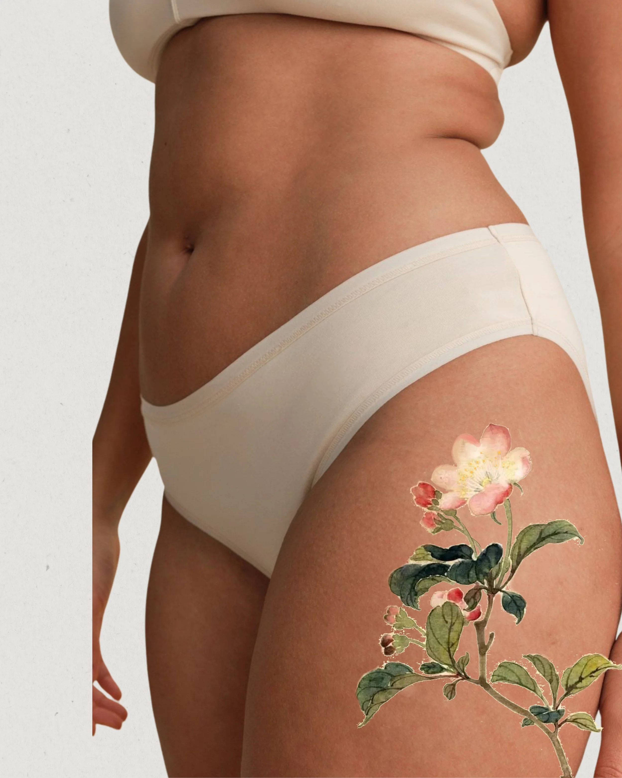 Close-up of a woman's midsection wearing beige underwear, with a floral tattoo on her upper thigh.