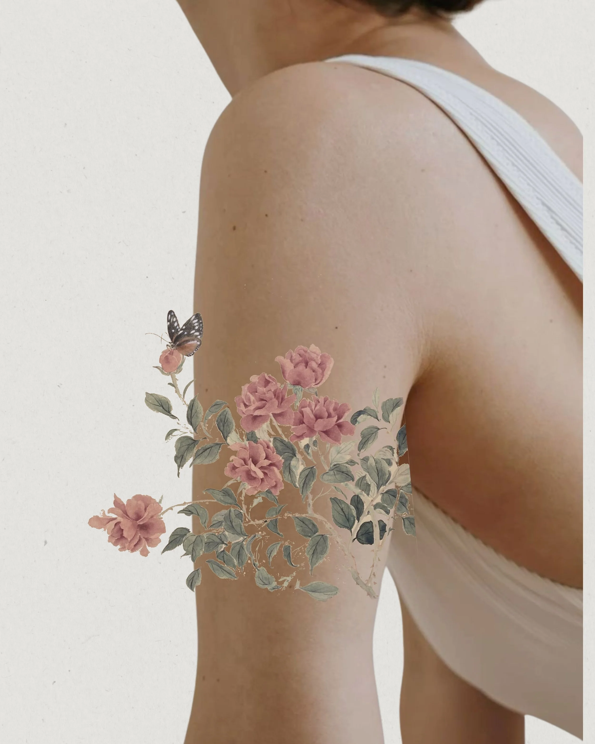 A woman wearing a white tank top showing her shoulder and upper arm, with a floral tattoo featuring pink flowers, green leaves, and a butterfly.