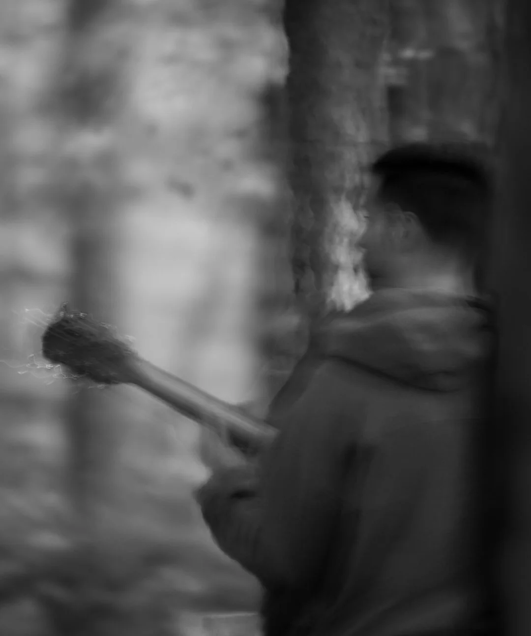 A young person wearing a hoodie and cap holding a sparkler in a blurry, grainy black-and-white photograph.